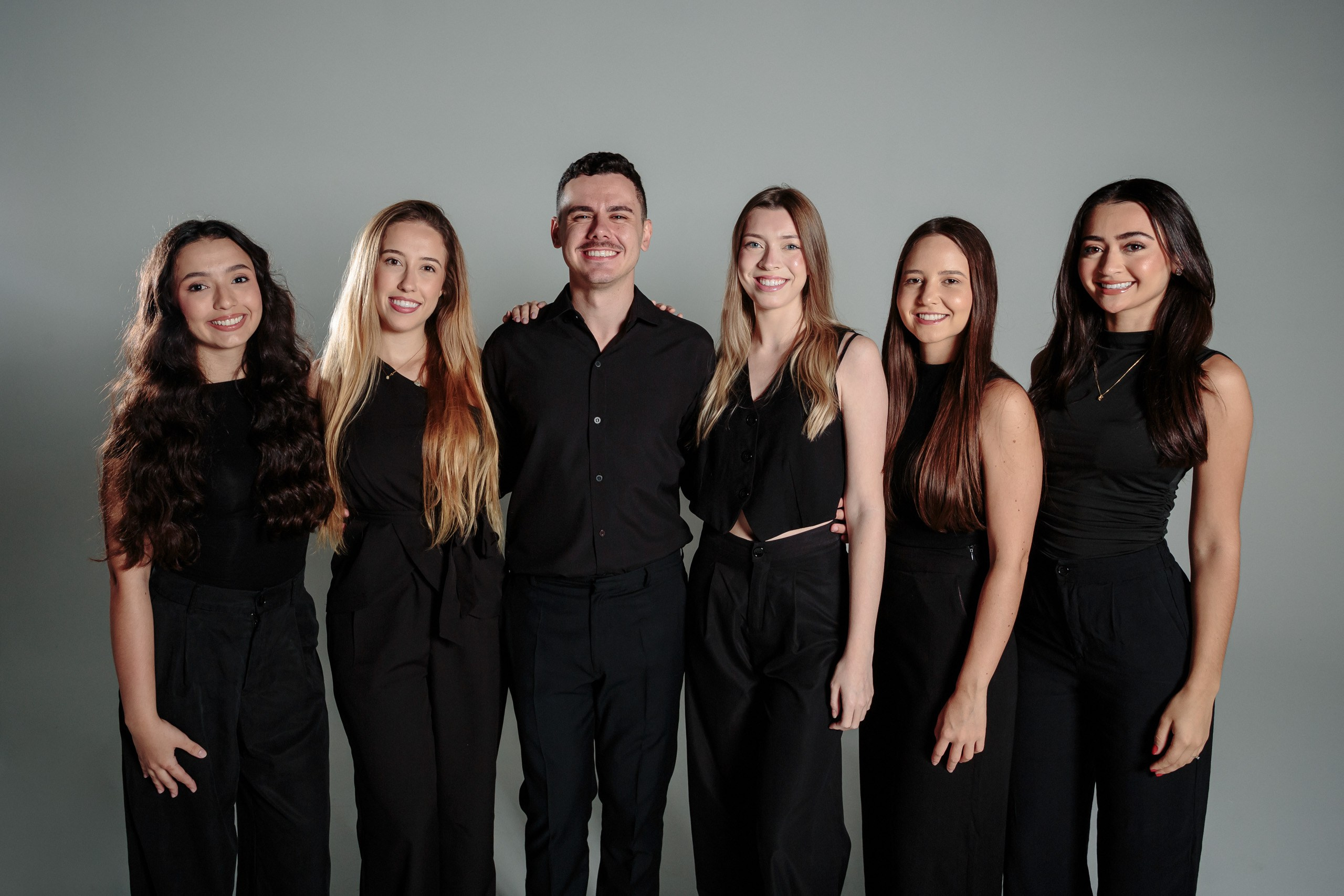 Ensaio de formatura em Balneário Camboriú; retrato em grupo de estúdio com o formando e colegas vestidos de preto, posando sorridentes.