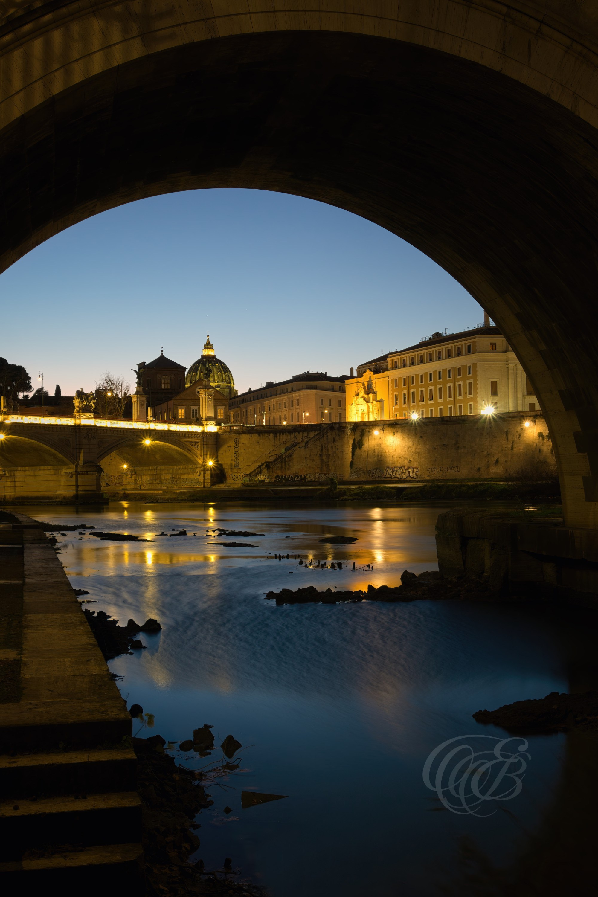 Rome, Italy – Blue hour view beneath Ponte Sant’Angelo with soft reflections on the Tiber River and historic bridge arches and statues in evening light – Eduardo Bartoli Photography.