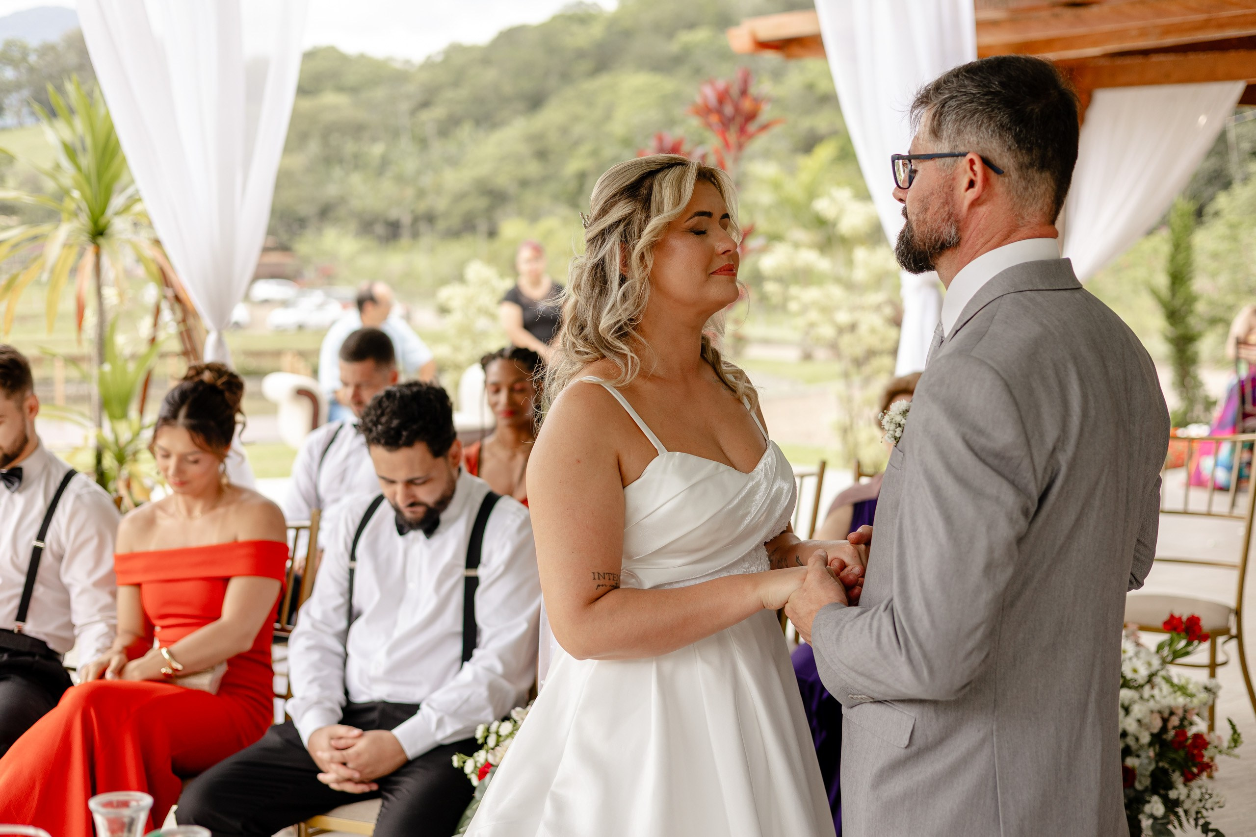 Fotógrafo de casamento em Santa Catarina; noivos de mãos dadas com os olhos fechados durante momento emocionante da cerimônia no campo.