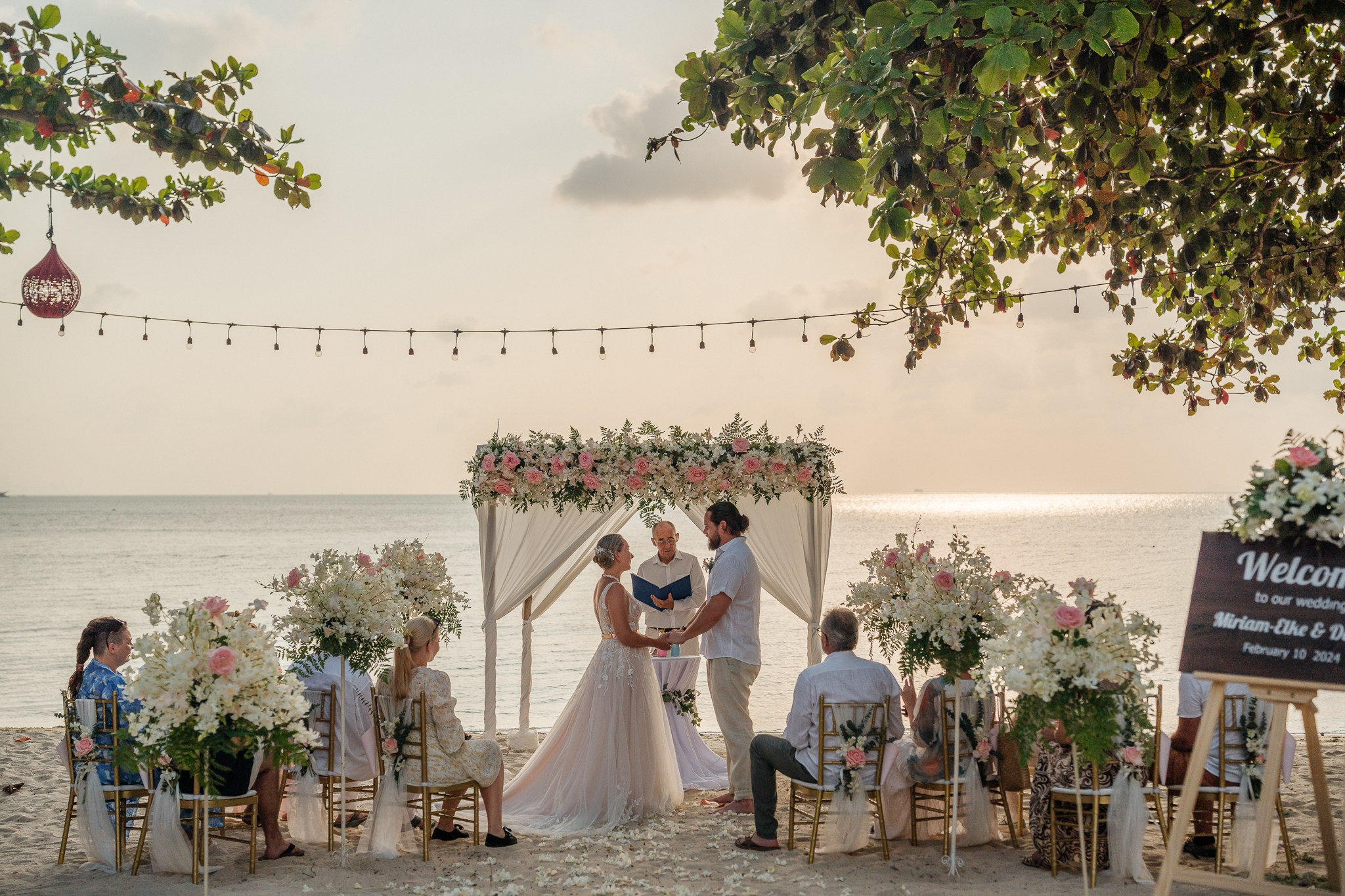 Bride and groom celebrating a beautiful beach wedding in Koh Samui, Thailand, surrounded by friends and family with tropical ocean views