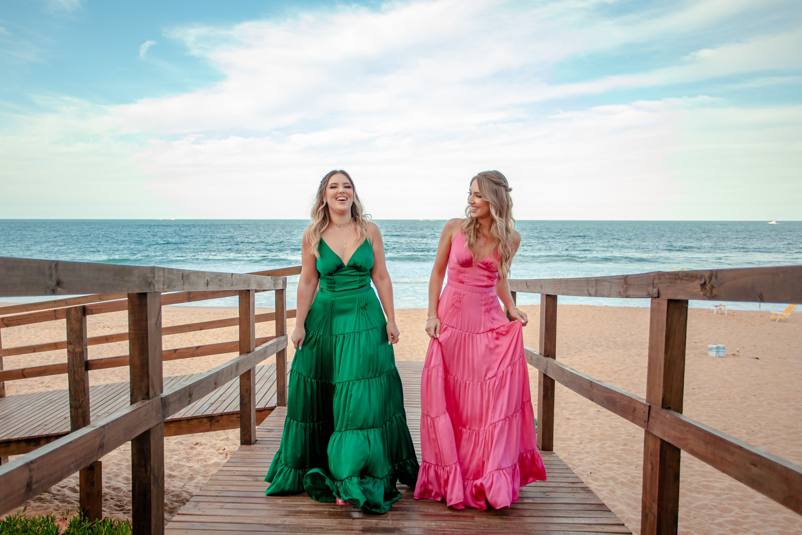 Fotógrafo festa de formatura em Balneário Camboriú; retrato descontraído e alegre das duas formandas a caminhar e conversar na passarela de madeira do Bali Bistro Beach.