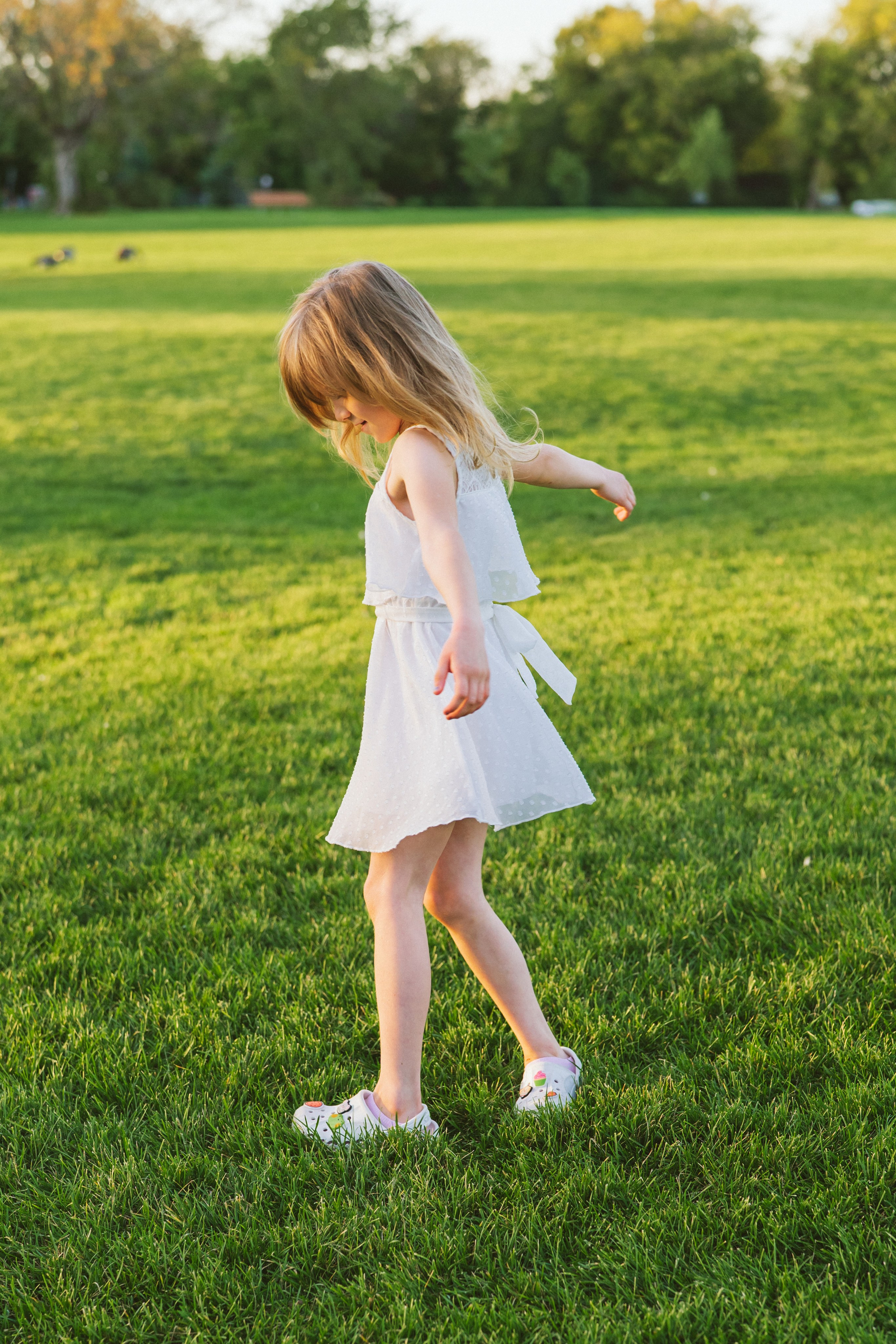 Little girl in a white dress spinning in the park