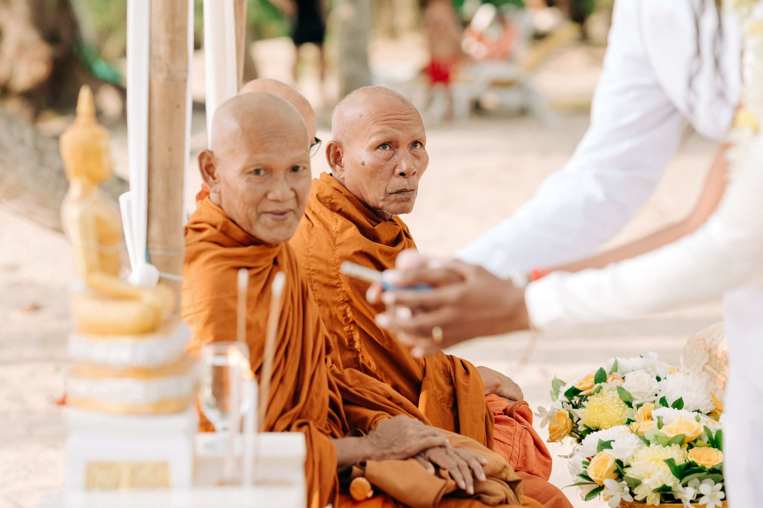 Couple taking part in a traditional Buddhist wedding ceremony on a tropical beach in Koh Samui, Thailand, with monks, flowers, and ocean views.