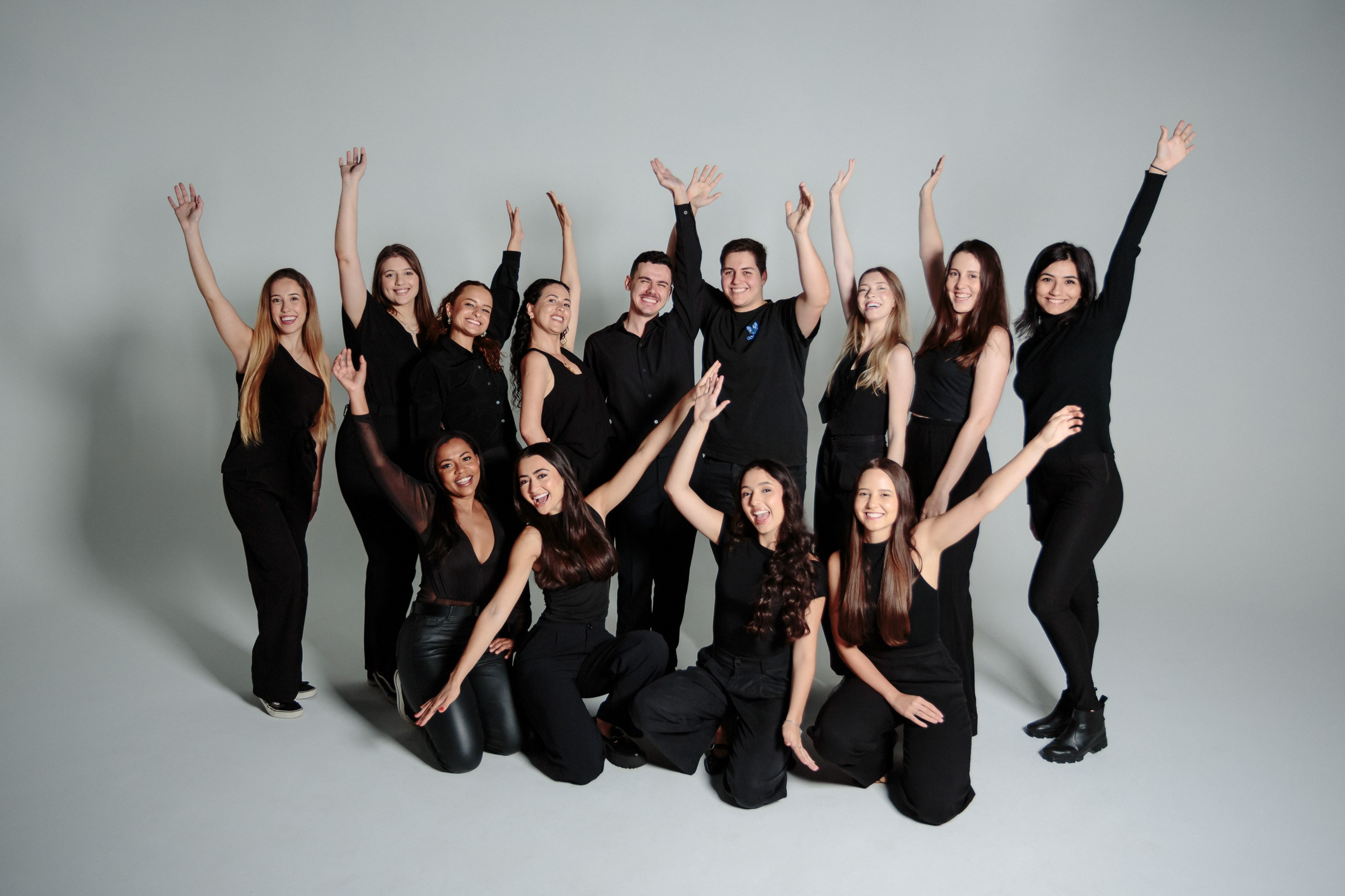 Ensaio de formatura de odontologia em Balneário Camboriú; turma completa de formandos vestidos de preto celebrando com braços erguidos e muita energia em estúdio.