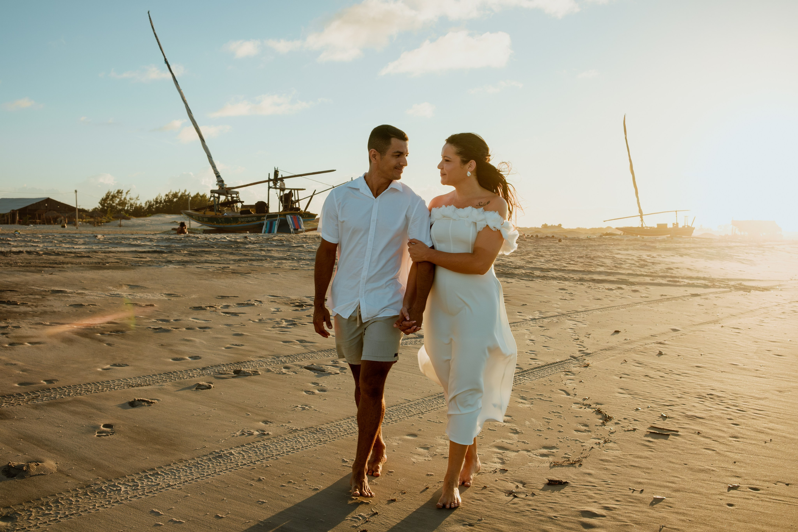 casal caminhando na praia, eles estão se olhando e sorrindo