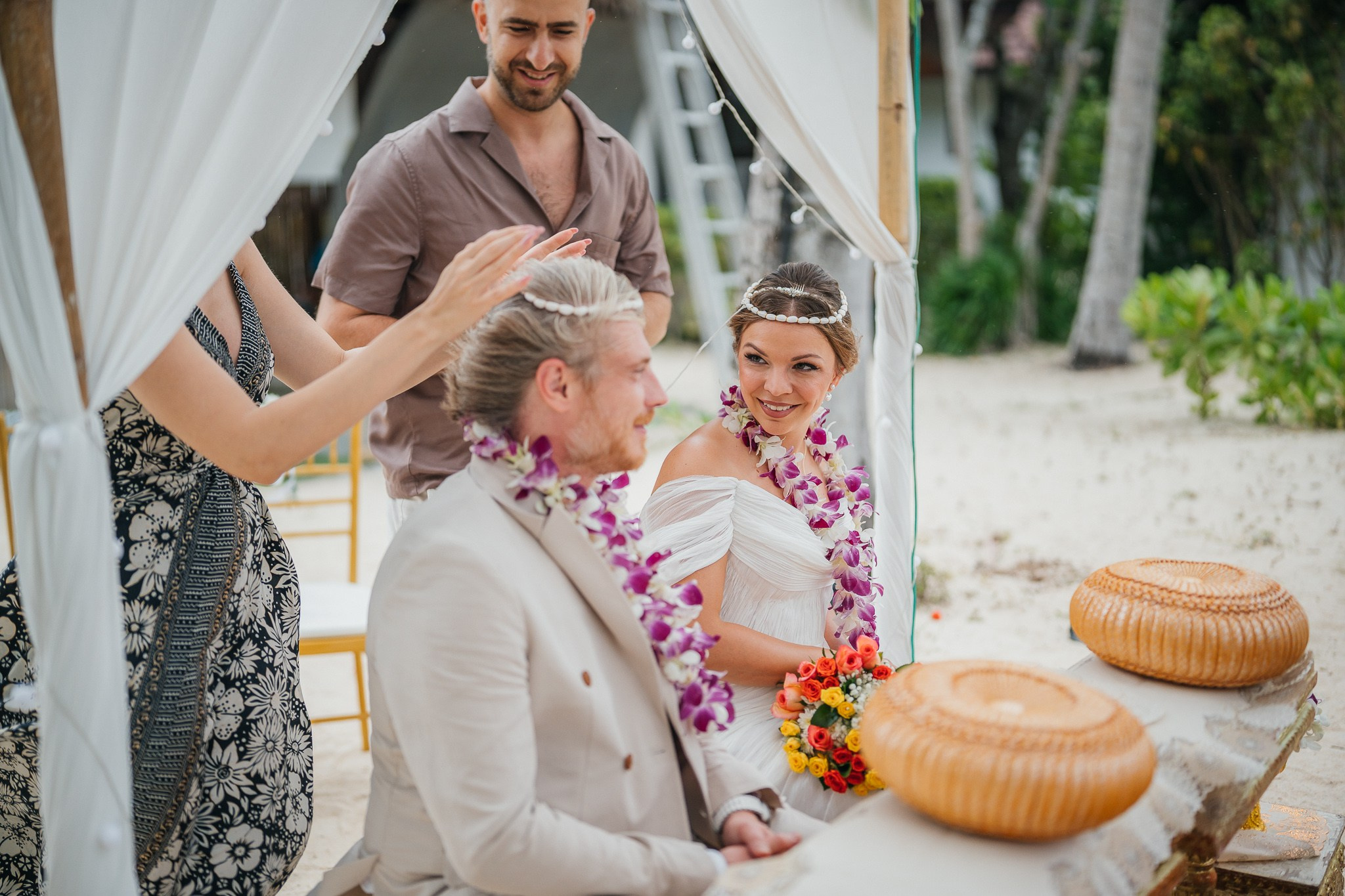 Couple taking part in a traditional Buddhist wedding ceremony on a tropical beach in Koh Samui, Thailand, with monks, flowers, and ocean views.