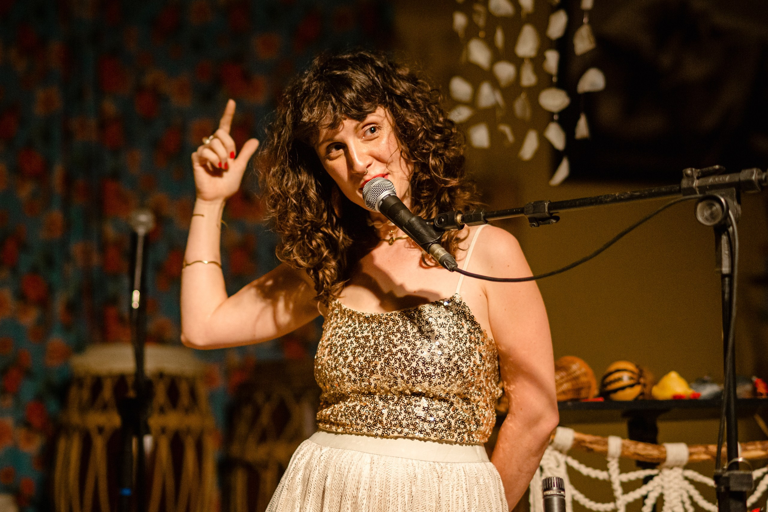 Fotógrafo de show em Balneário Camboriú; a cantora Joana Gaia apontando para cima enquanto canta ao vivo no bairro da Barra para a divulgação do álbum "Água Brasileira".