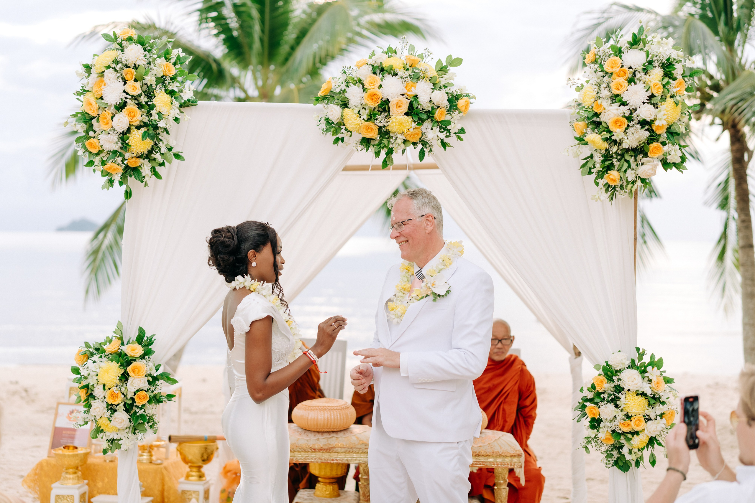Newlywed couple celebrating a Buddhist wedding ceremony on a beautiful beach in Koh Samui, Thailand.