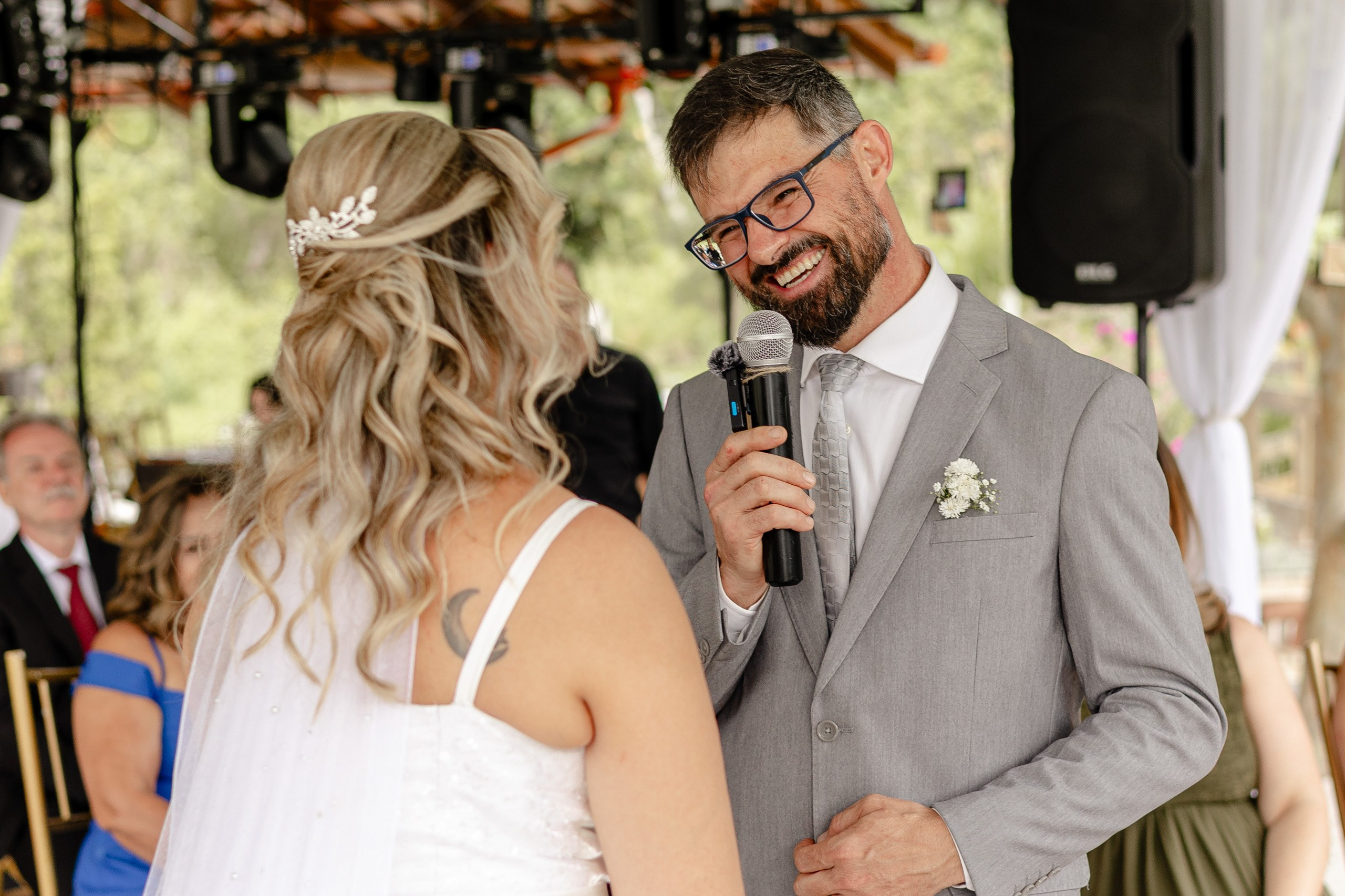 Fotógrafo de casamento em Santa Catarina; noivo sorridente falando ao microfone olhando para a noiva durante a cerimônia no campo.