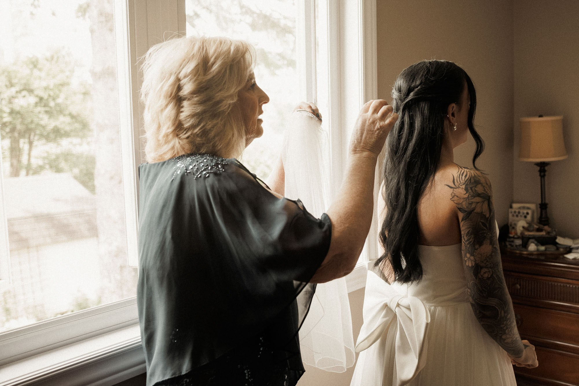A family member adjusts the bride’s hair by a window before a Greater Montreal wedding.