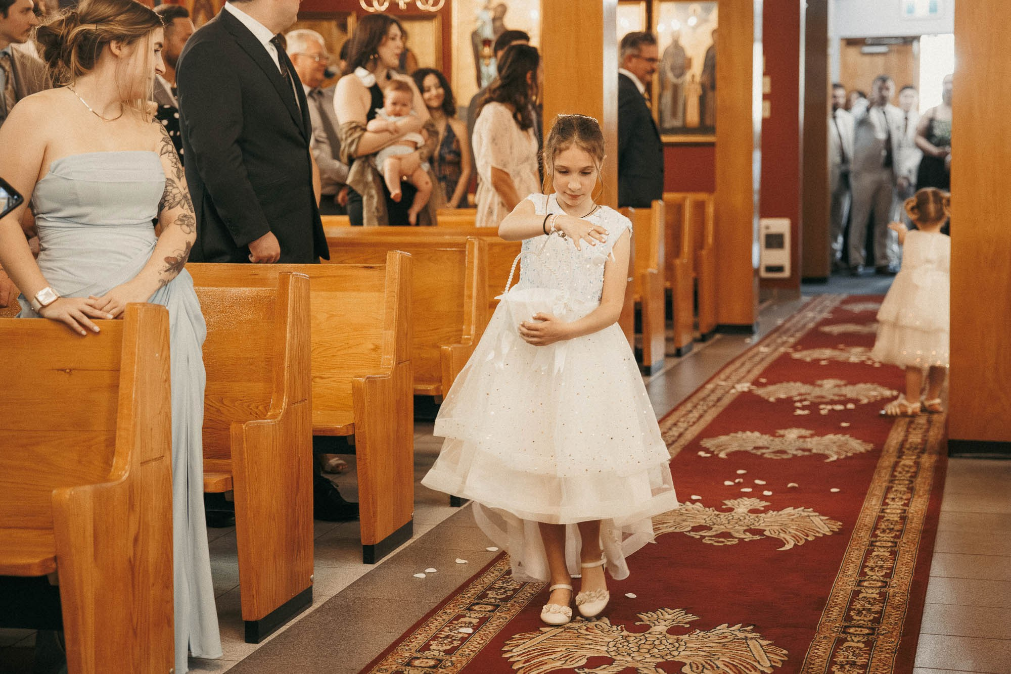 A young flower girl scatters petals along the church aisle.