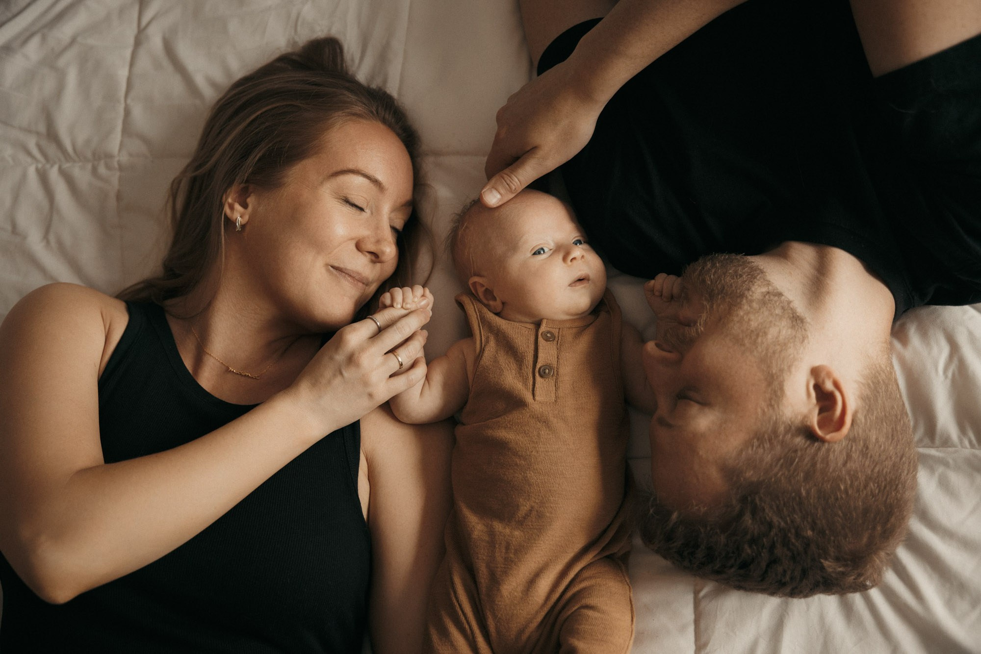 Parents allongés avec leur nouveau-né lors d’une séance photo à domicile à Montréal