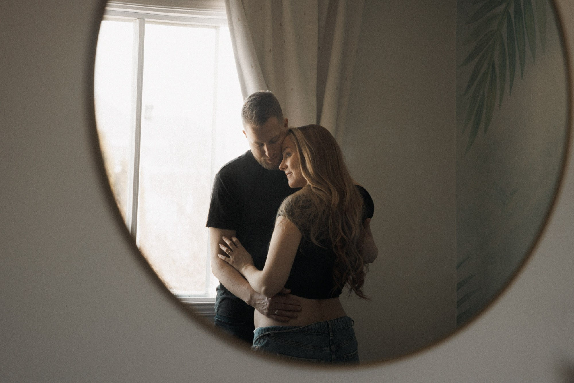 Expecting couple reflected in a round mirror during an at-home session