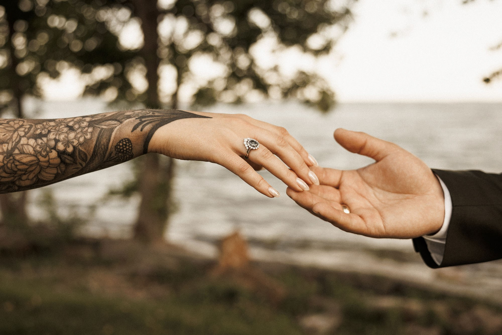 The bride’s tattooed hand reaches toward the groom, her ring visible.
