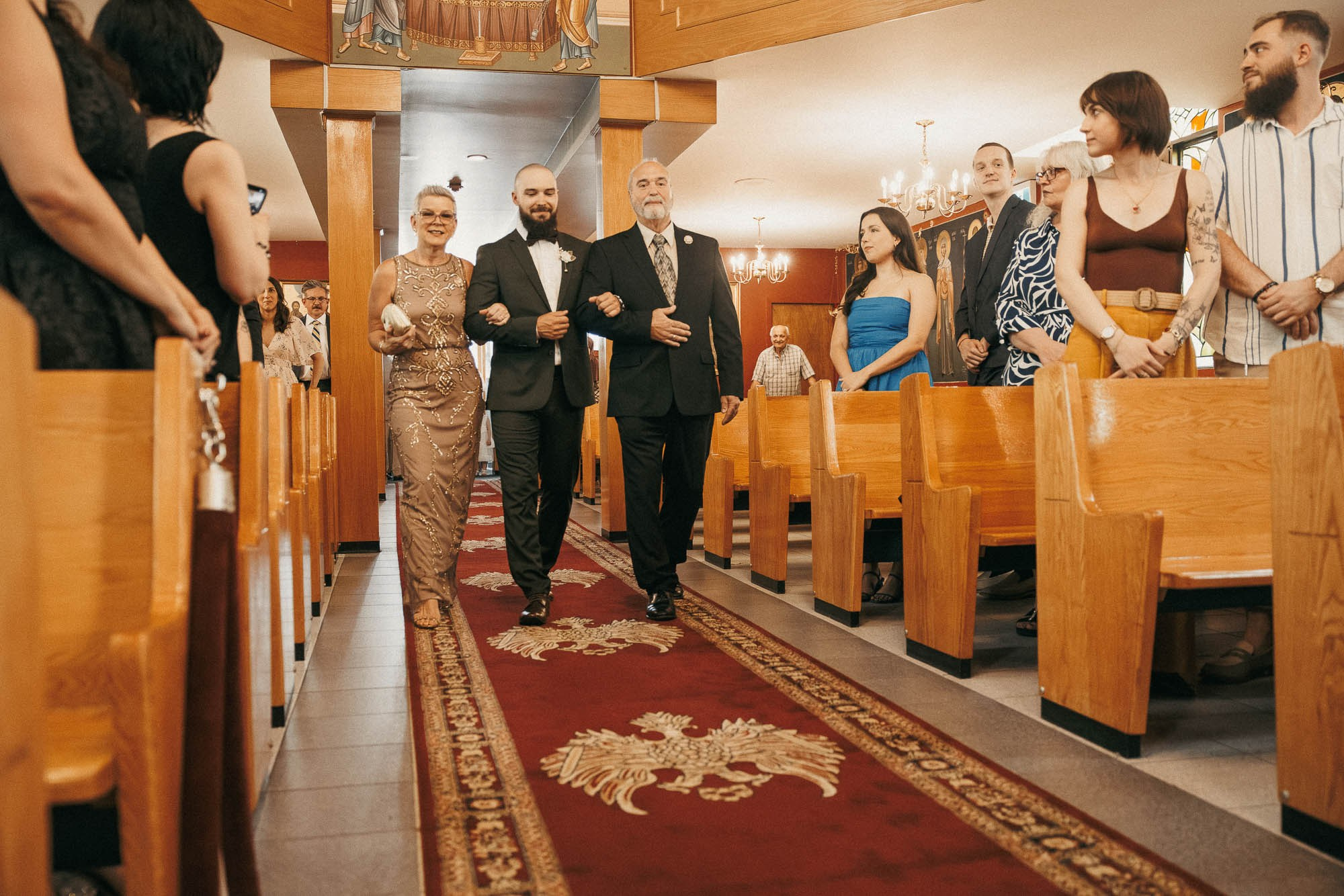 The groom walks down the church aisle with his parents.