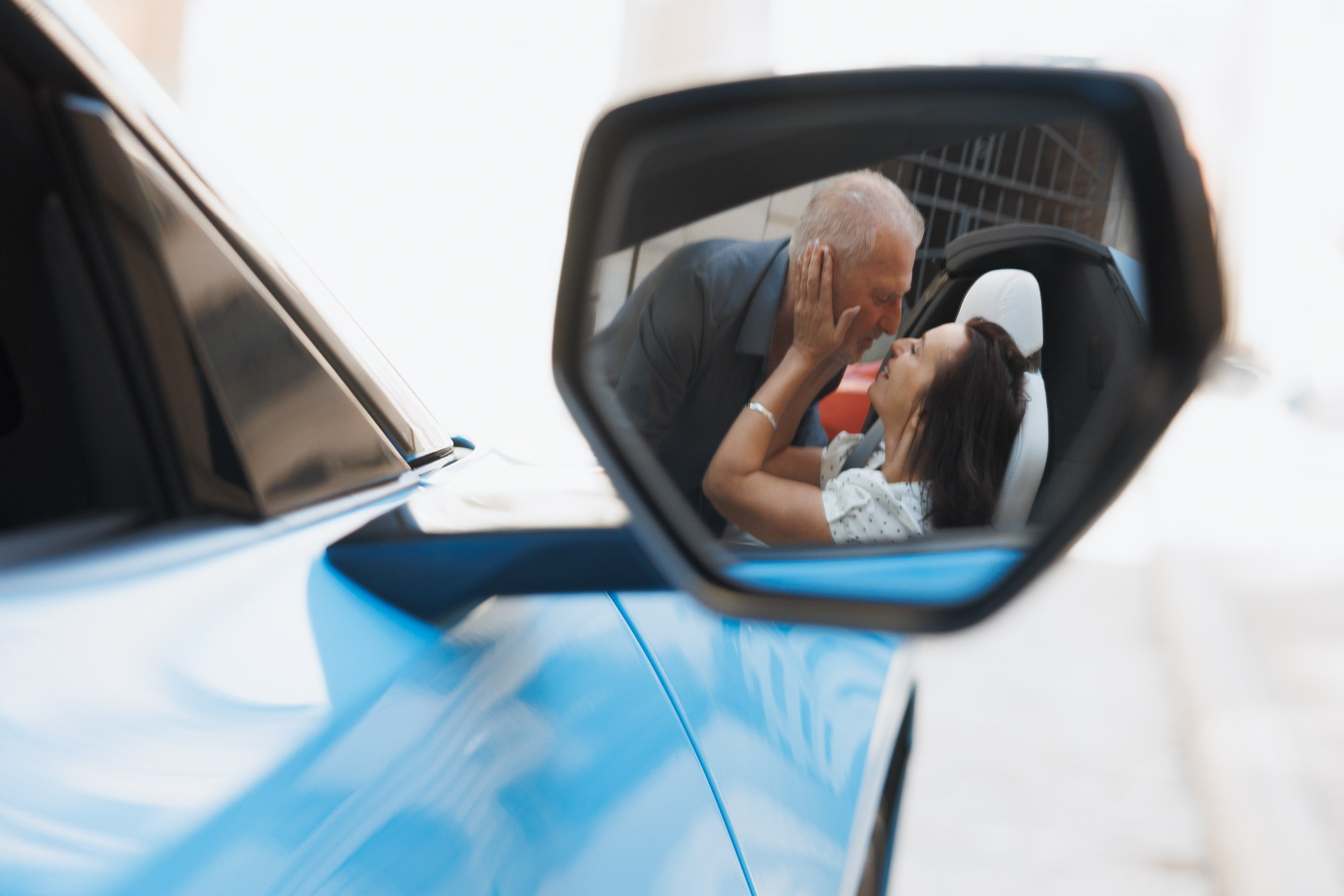 Couple kissing in the side mirror of a blue convertible