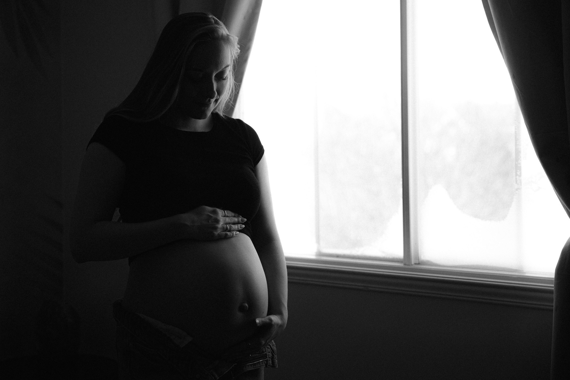 Black-and-white silhouette of an expectant mother beside a window