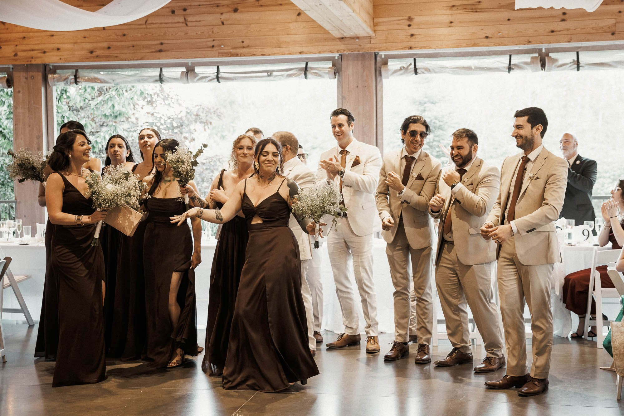 Wedding party members dance into the reception as guests applaud.