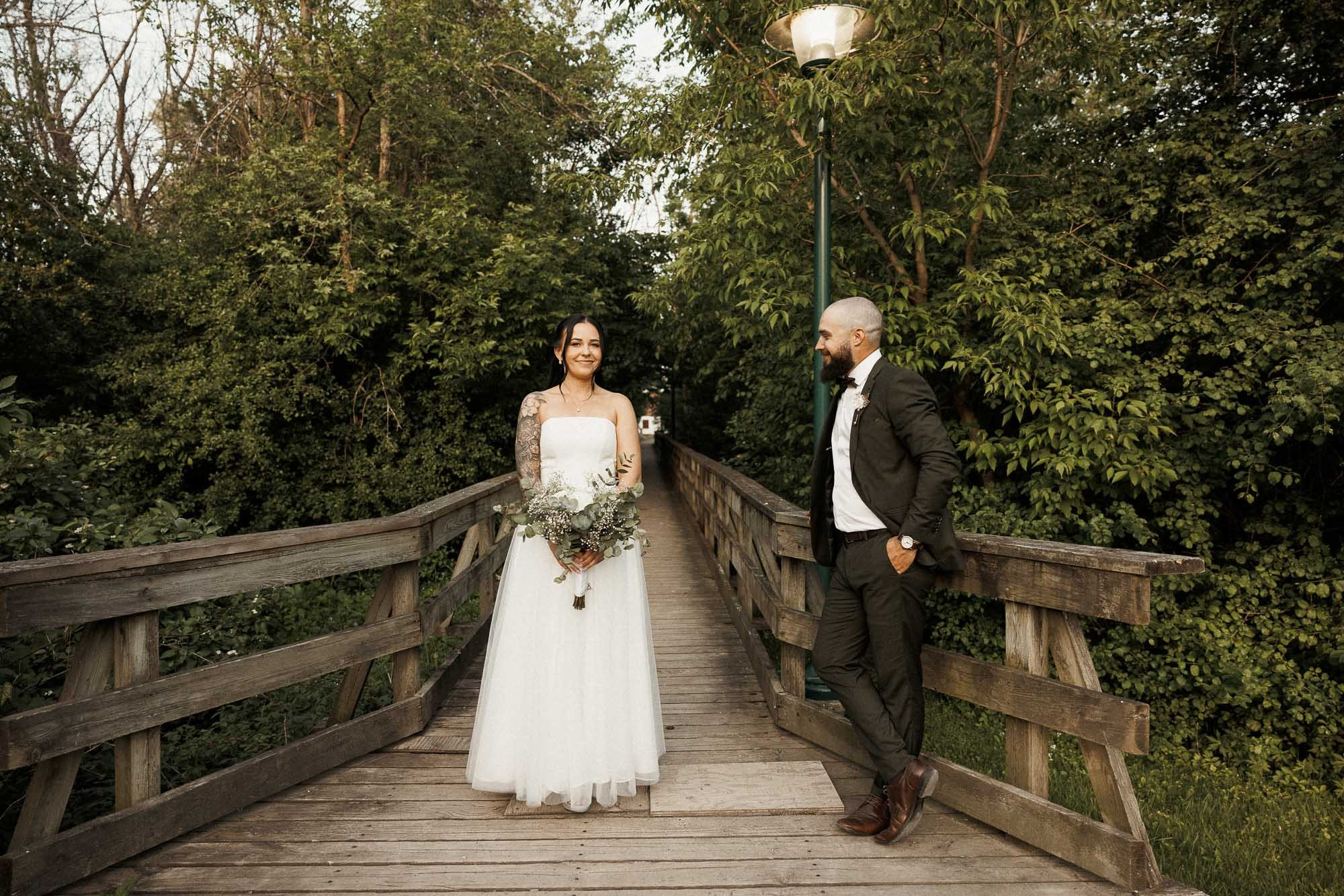 Kendyl and Mikey pose on a wooden bridge surrounded by greenery.