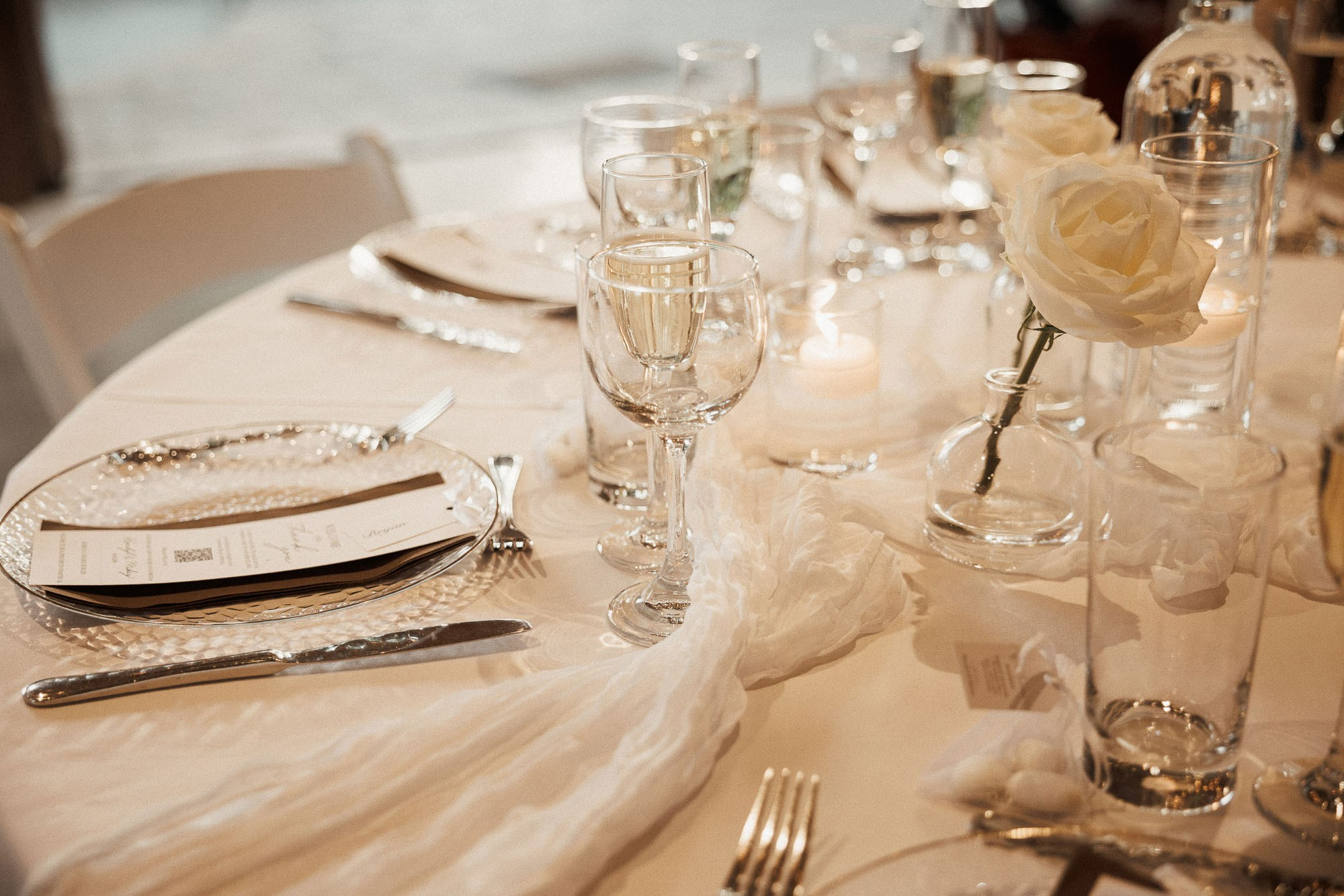 Wedding table setting with glassware, candles and white roses.