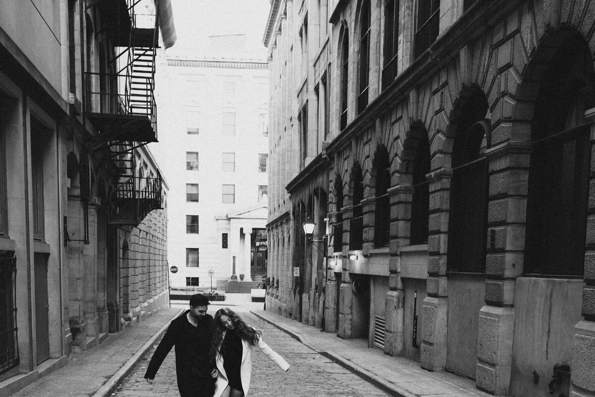 Black-and-white photograph of a couple running down a cobblestone street in Old Montreal