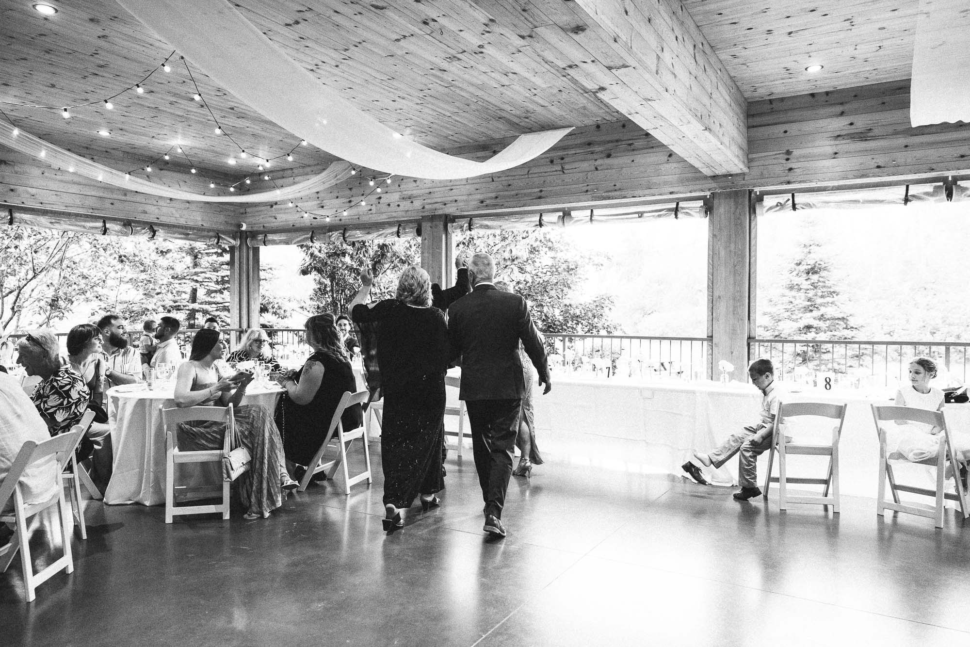 Guests cross the dance floor in a black-and-white view of the rustic reception.
