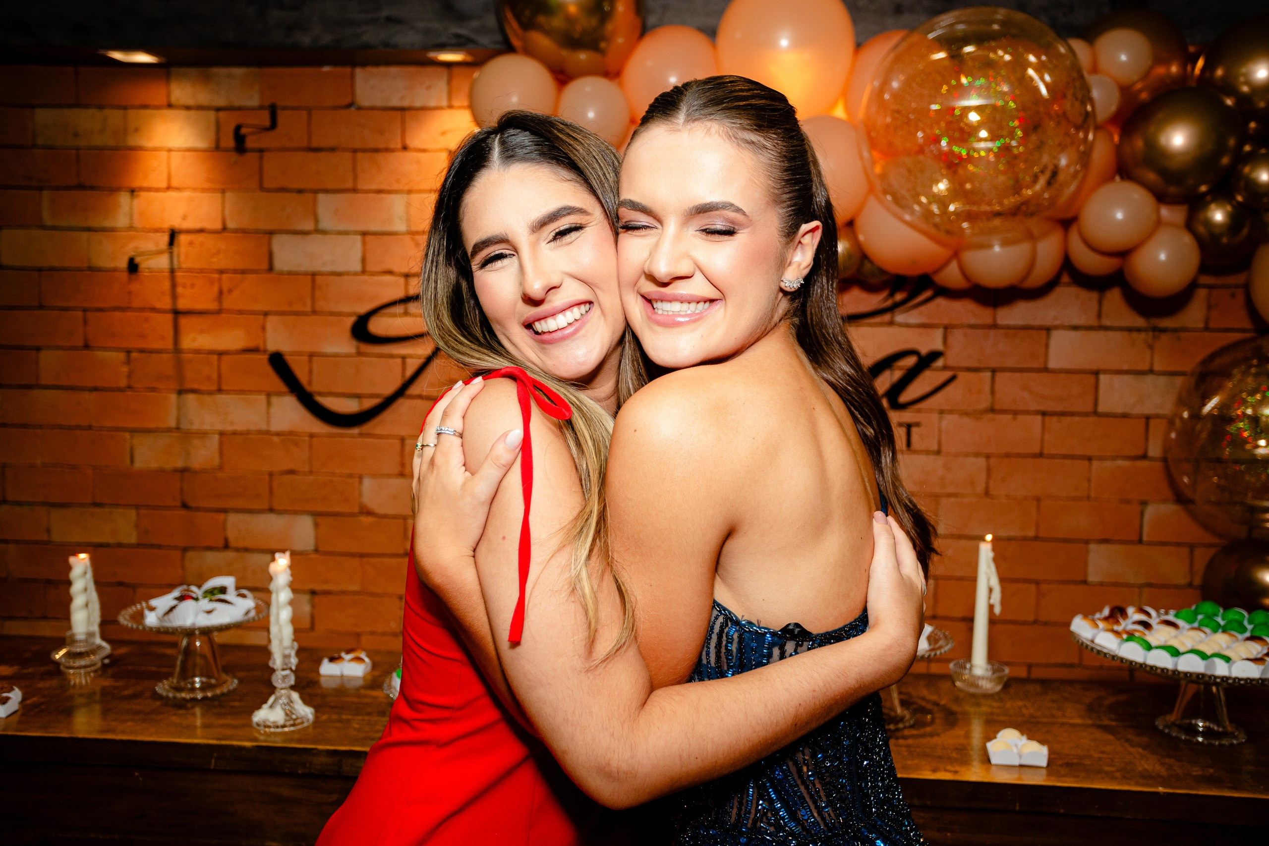 Fotógrafo de formatura em Balneário Camboriú; a formanda e uma convidada compartilham um abraço afetuoso e sorridente durante a festa com decoração de balões.