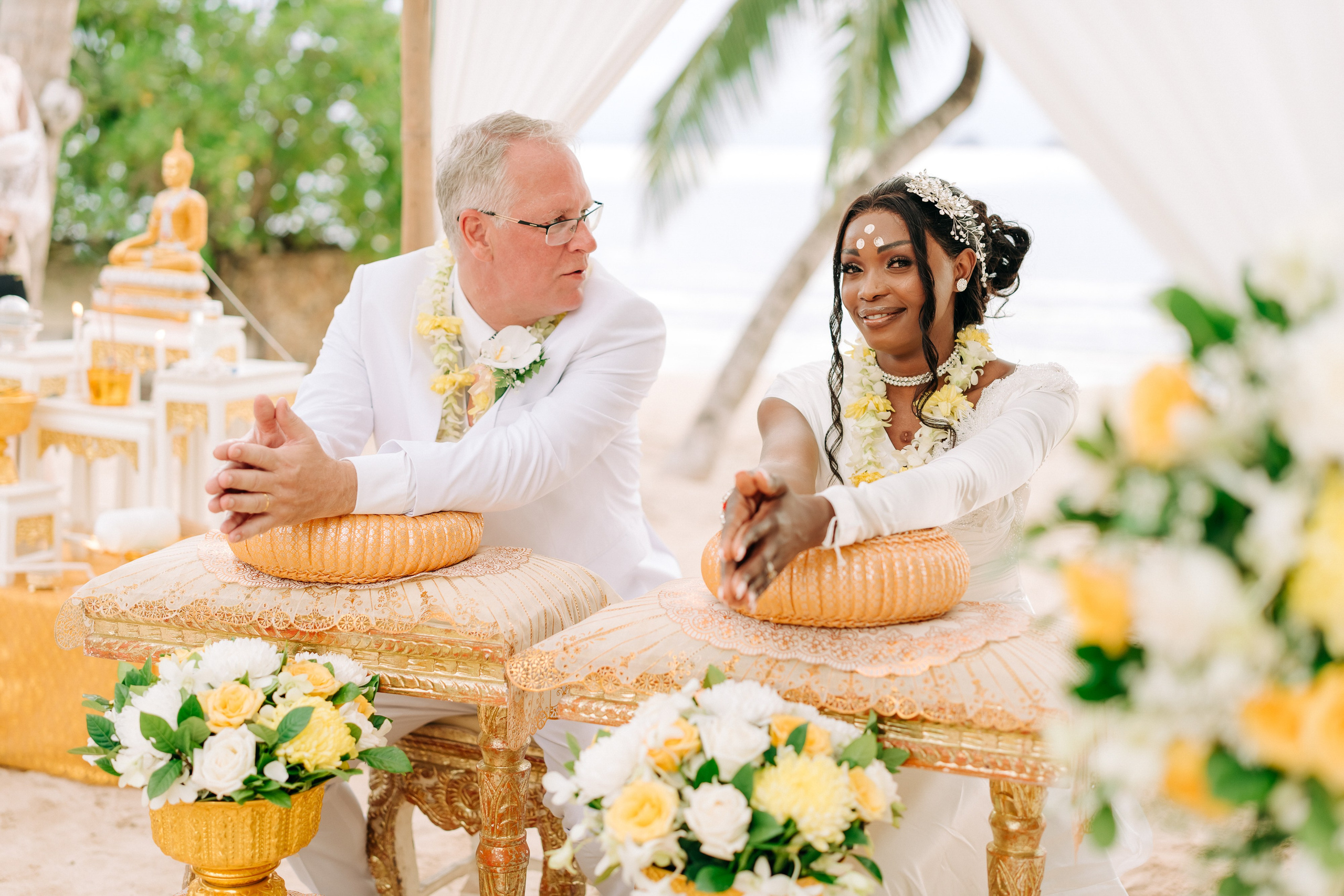 Couple taking part in a traditional Buddhist wedding ceremony on a tropical beach in Koh Samui, Thailand, with monks, flowers, and ocean views.