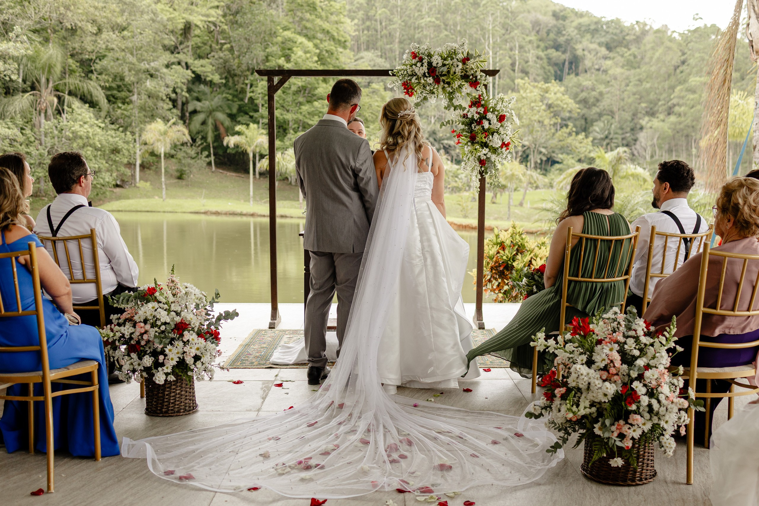 Fotógrafo de casamento em Santa Catarina; vista aberta da cerimônia ao ar livre à beira do lago, com convidados sentados e casal no altar decorado.