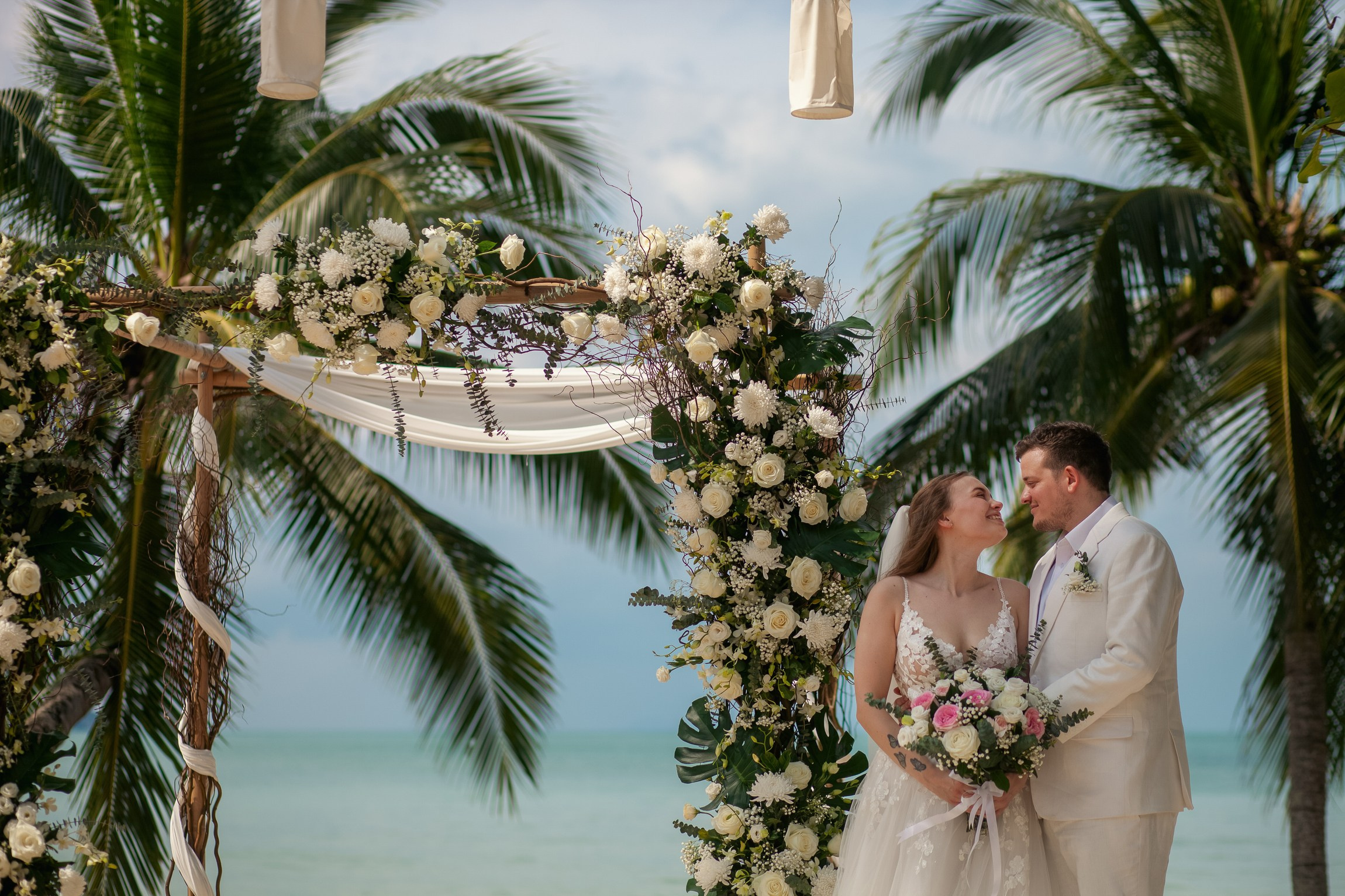 Romantic destination wedding on Koh Samui beach with tropical flowers, ocean views and happy newlyweds