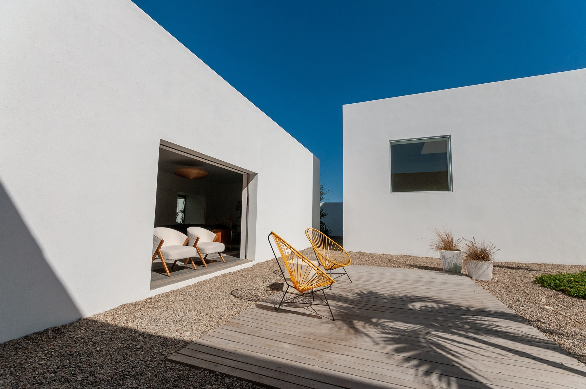 Minimalist white exterior home in Todos Santos . Clean volumes, garden lounge area and palm shadows, luxury real estate photography