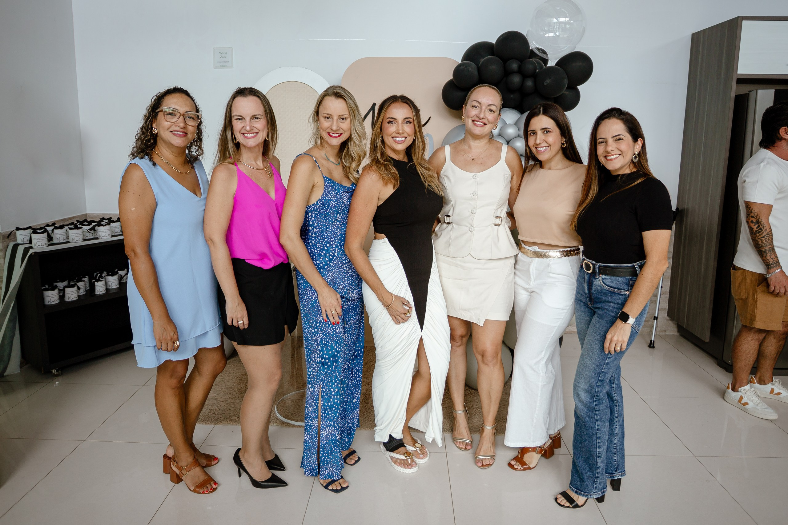 Fotografia de cobertura de festa de aniversário em Itajaí mostrando a aniversariante sorridente posando ao lado de suas amigas e convidadas em frente ao painel decorado.