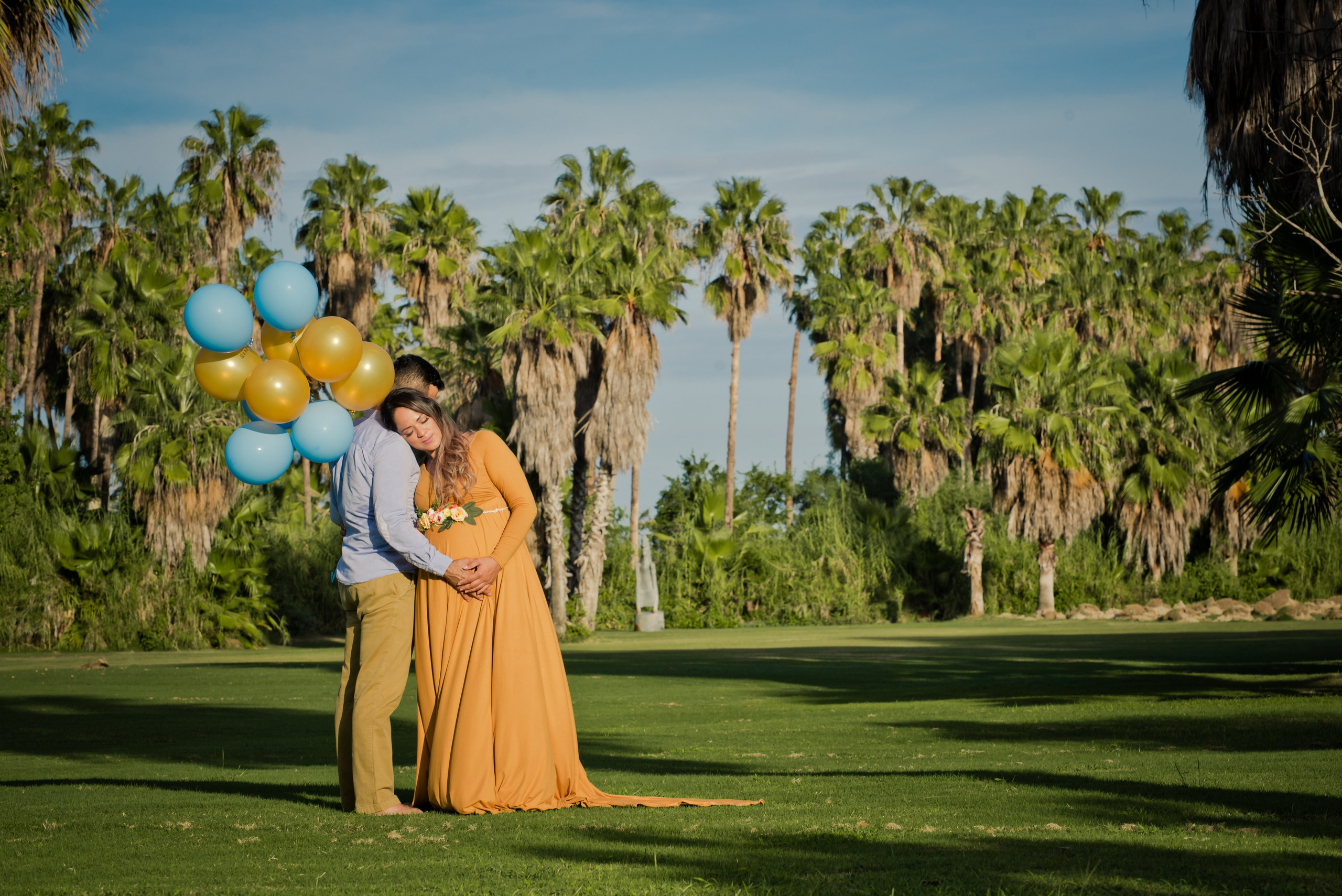 Maternity couple photoshoot in Los Cabos – expecting parents embracing by the ocean, hands on baby bump, with palm trees and beach backdrop, captured by Baja California Sur photographer