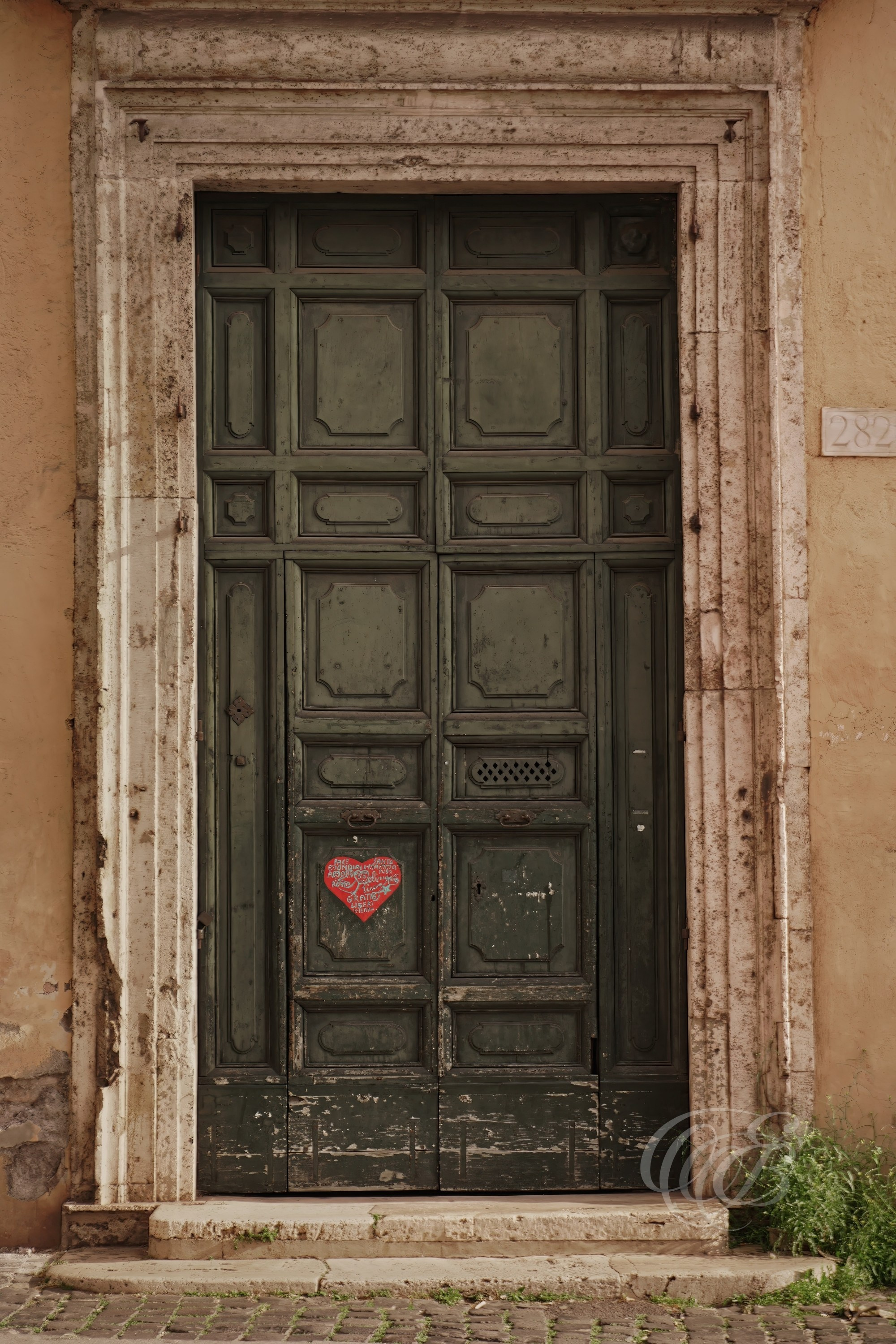 Street Photography — Rome, Italy — Old Door + Heart — Aged Roman doorway marked by a small heart, bringing together weathered textures, traces of time, and a subtle human gesture within the streets of the city — Eduardo Bartoli Photography.