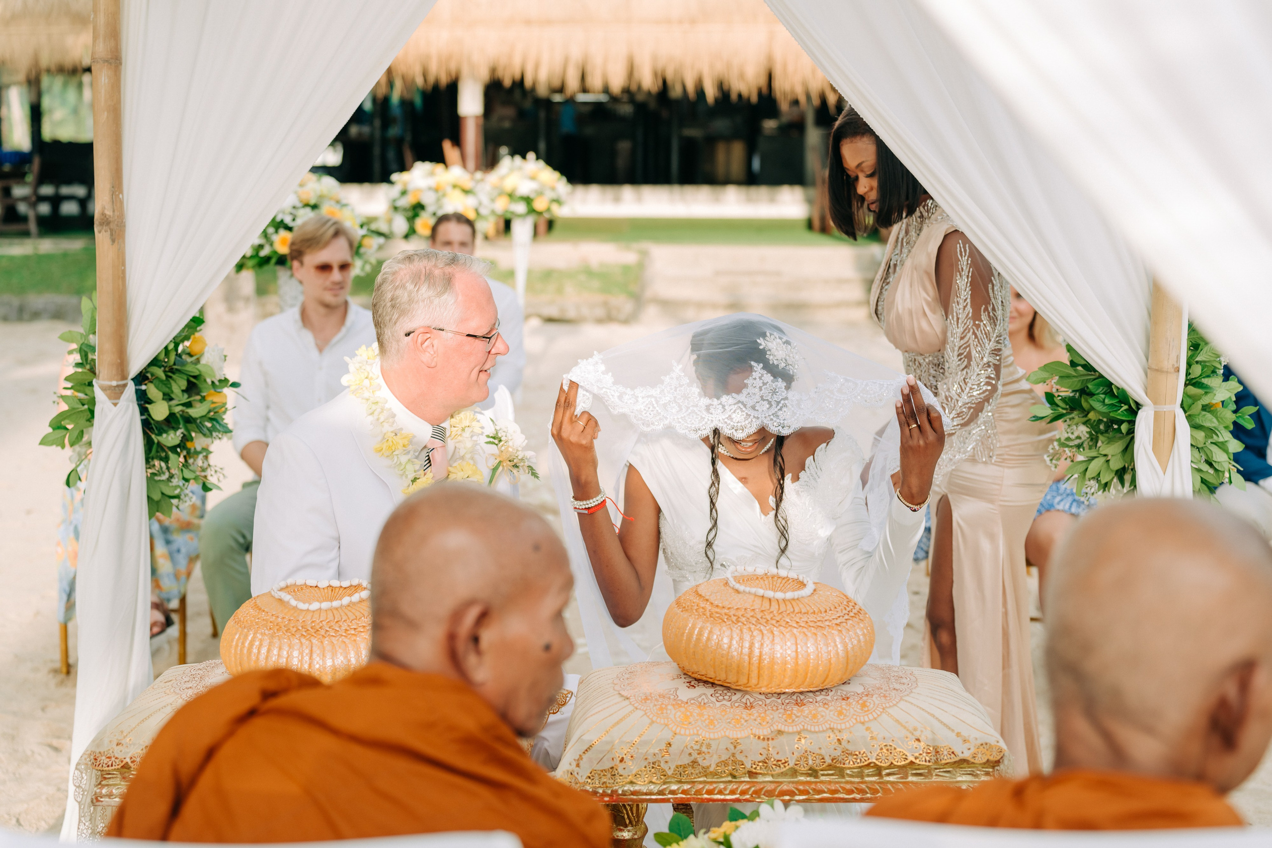 Couple taking part in a traditional Buddhist wedding ceremony on a tropical beach in Koh Samui, Thailand, with monks, flowers, and ocean views.