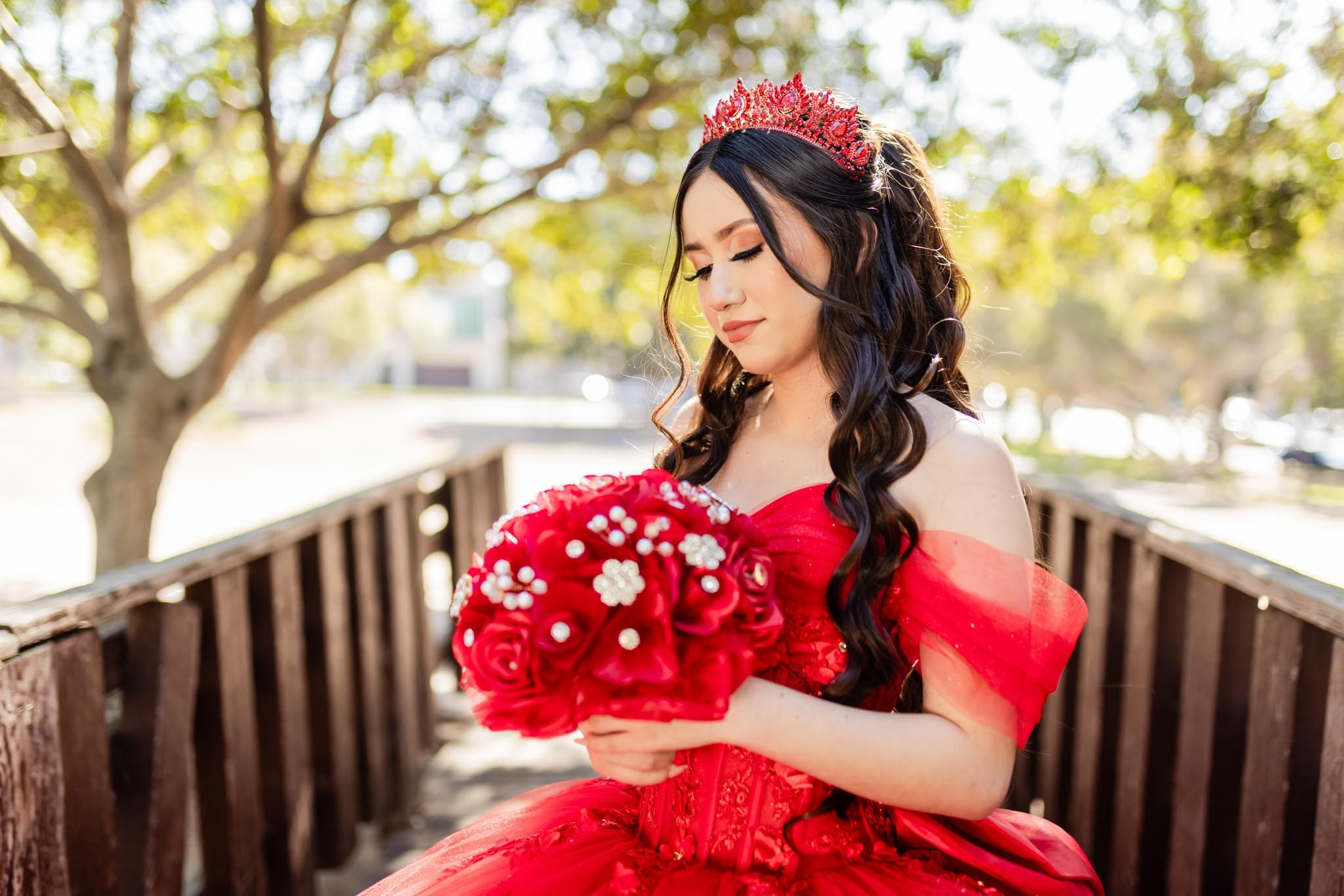 Quinceanera sentada en banca de madera con vestido rojo en sesion de fotos en exterior en Tijuana luz natural