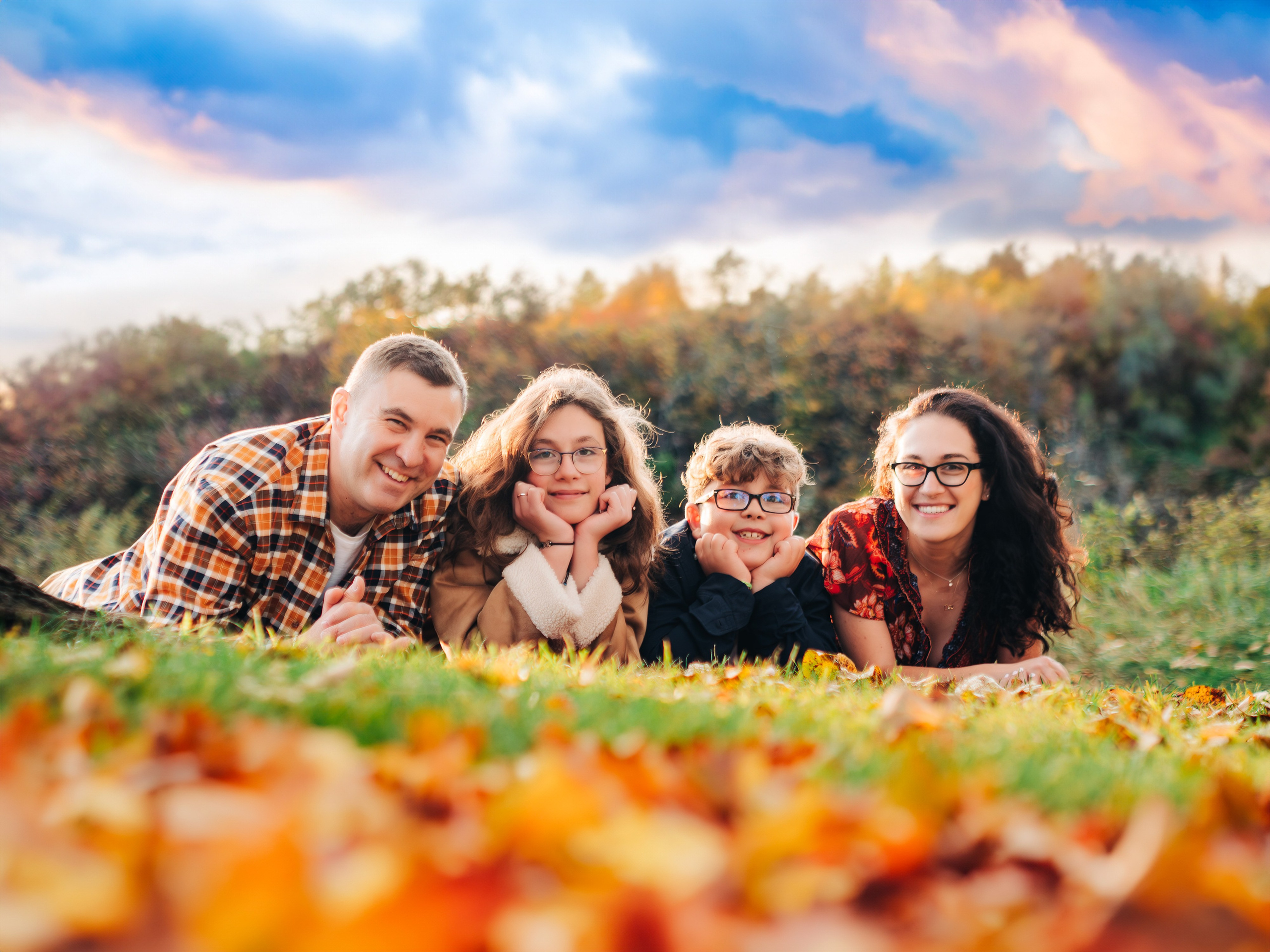 Spruce Grove family portrait photographer Dimitri Studio. Family smiling and laying in colorful fall leaves. Visit dimitristudio.com for professional photography.