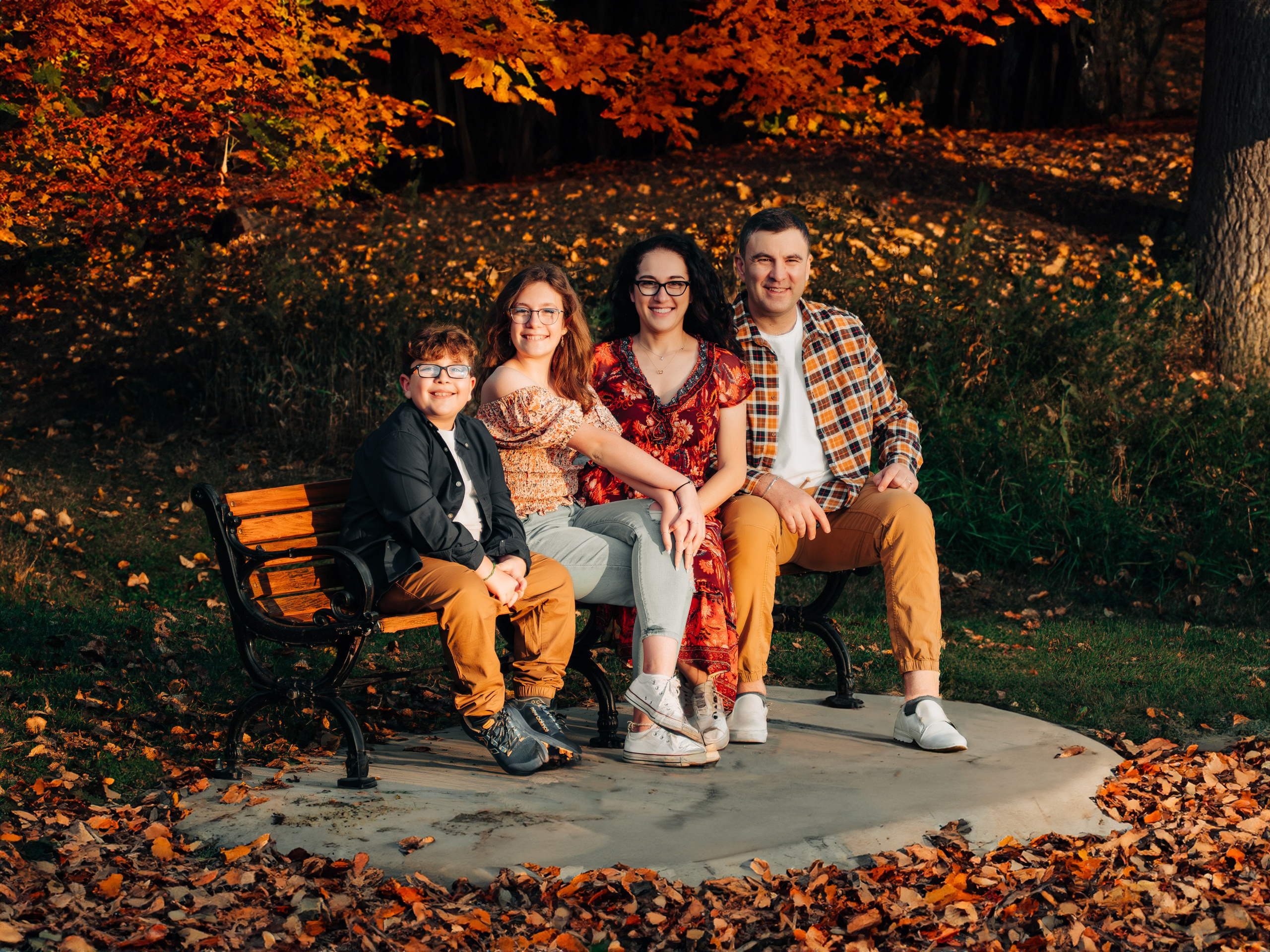 Professional family photography in Spruce Grove by Dimitri Studio. Happy family sitting on a park bench surrounded by autumn leaves. Book your session at dimitristudio.com