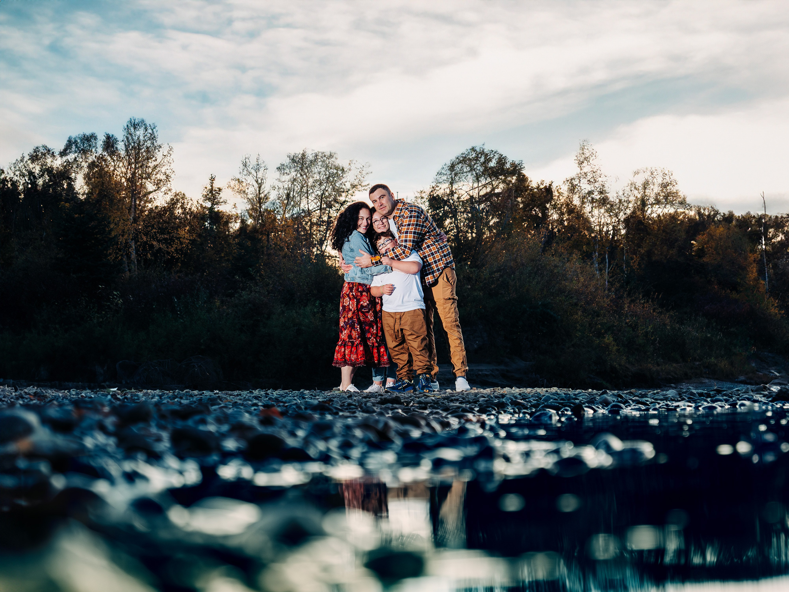 Family sunset photoshoot in Spruce Grove by Dimitri Studio. Family hugging on a scenic riverbank with autumn trees. Book now at dimitristudio.com