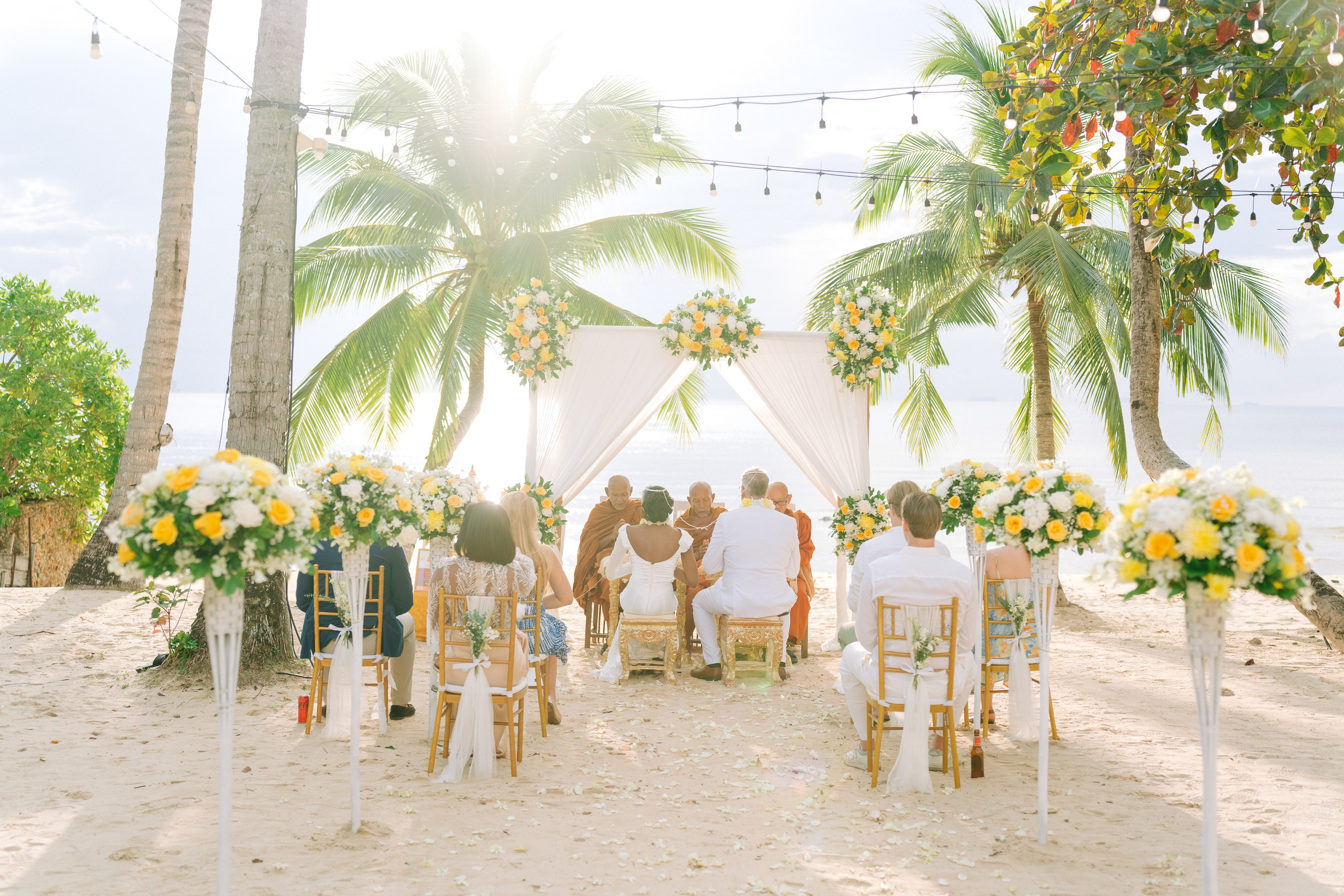 Bride and groom participating in a sacred Buddhist blessing ceremony by the sea in Koh Samui, Thailand.
