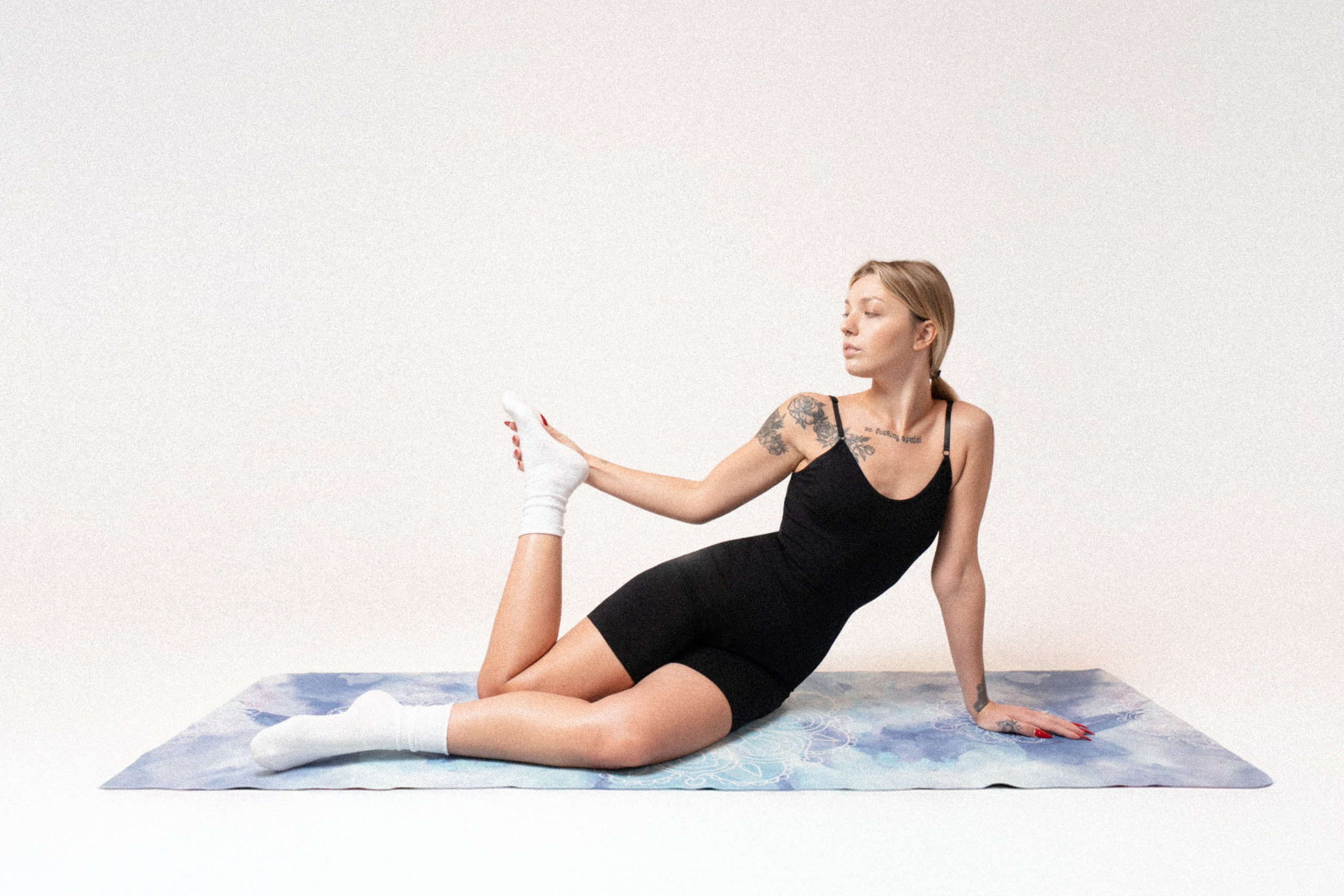 Young woman in black activewear stretching on a yoga mat in a bright minimalist studio.
