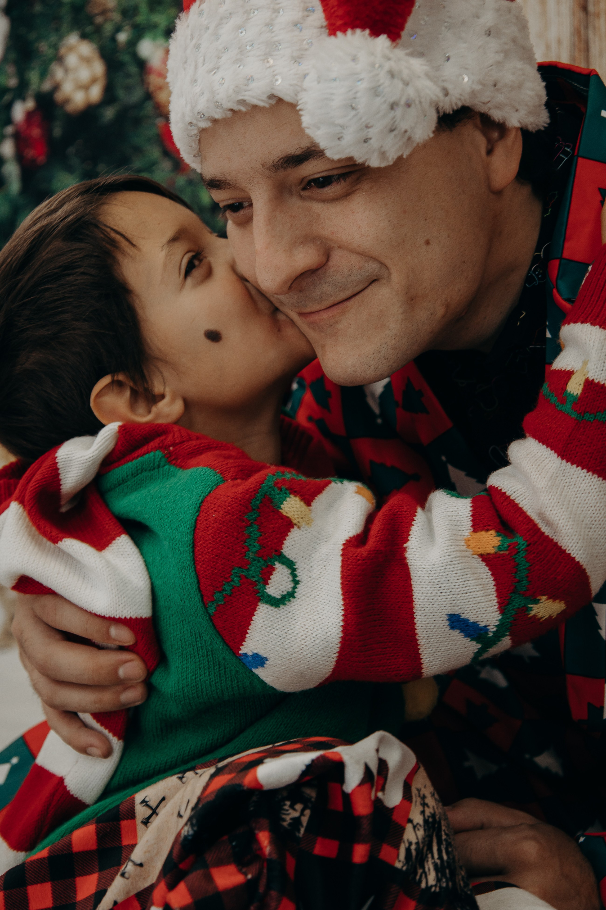 Young child kissing his father on the cheek in a warm, candid Christmas family portrait.