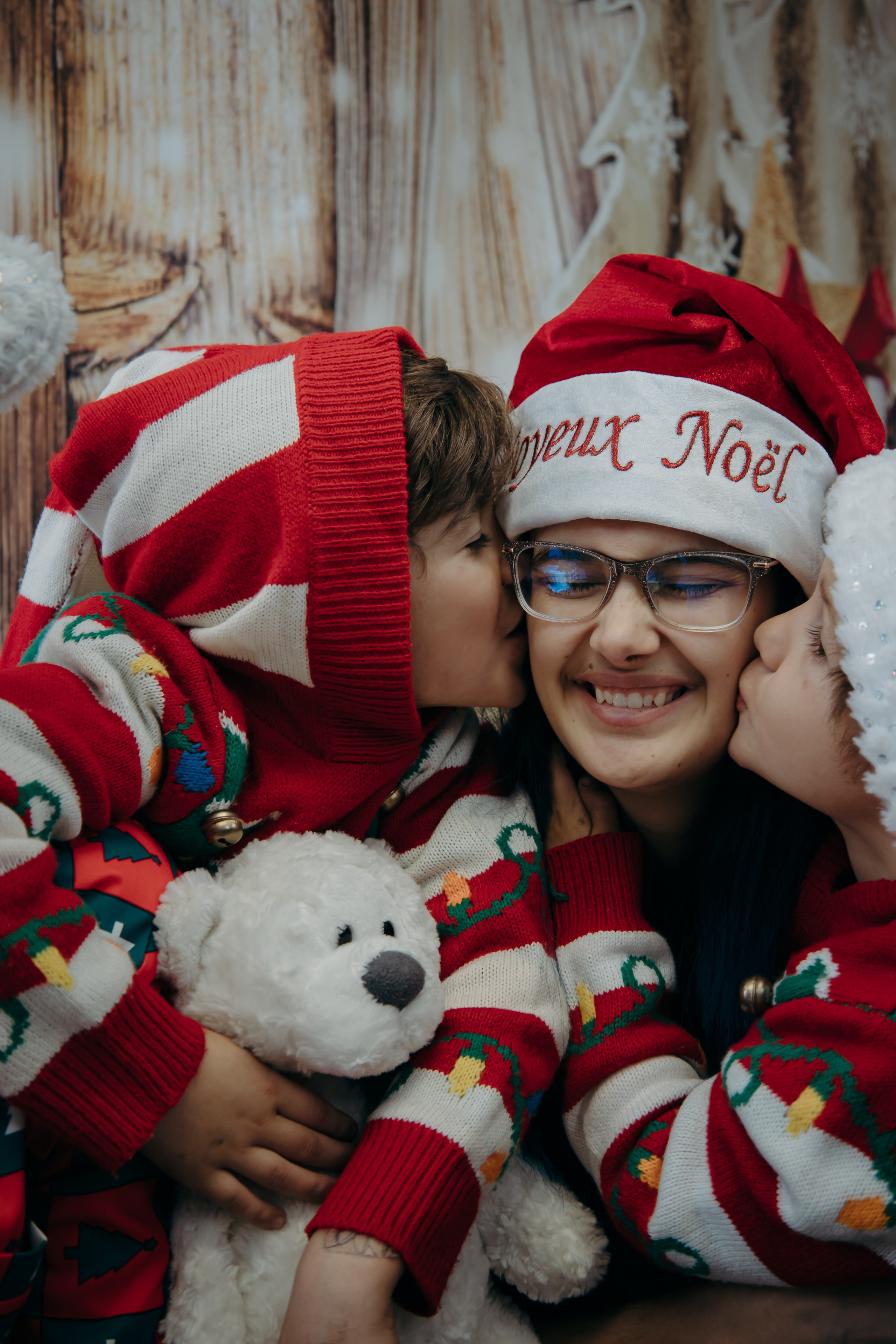 Smiling child in a red Christmas sweater holding a white teddy bear during a Christmas mini session in Calgary.