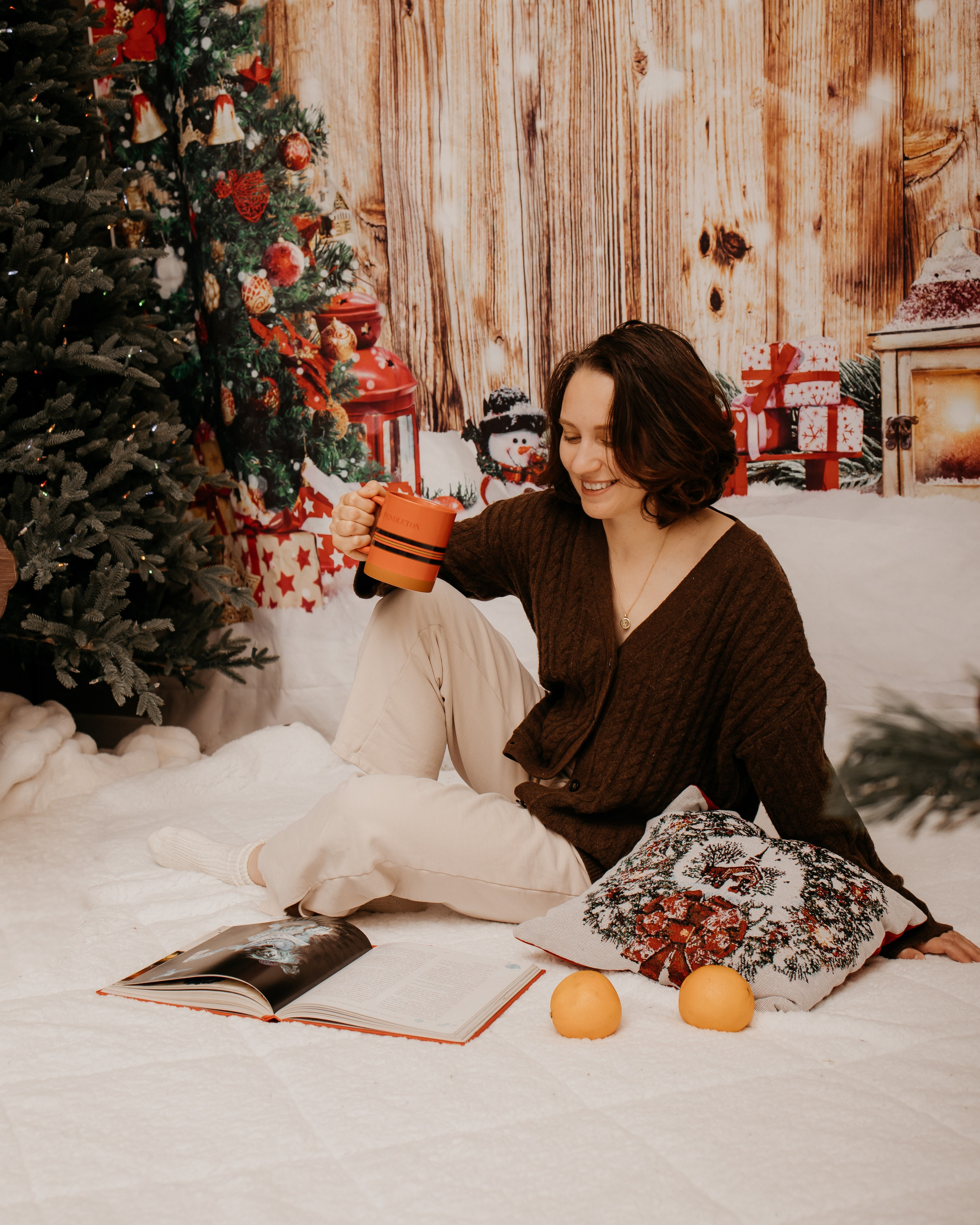 Woman sitting beside a Christmas tree with a warm mug, book, and festive decorations in a Calgary home studio.