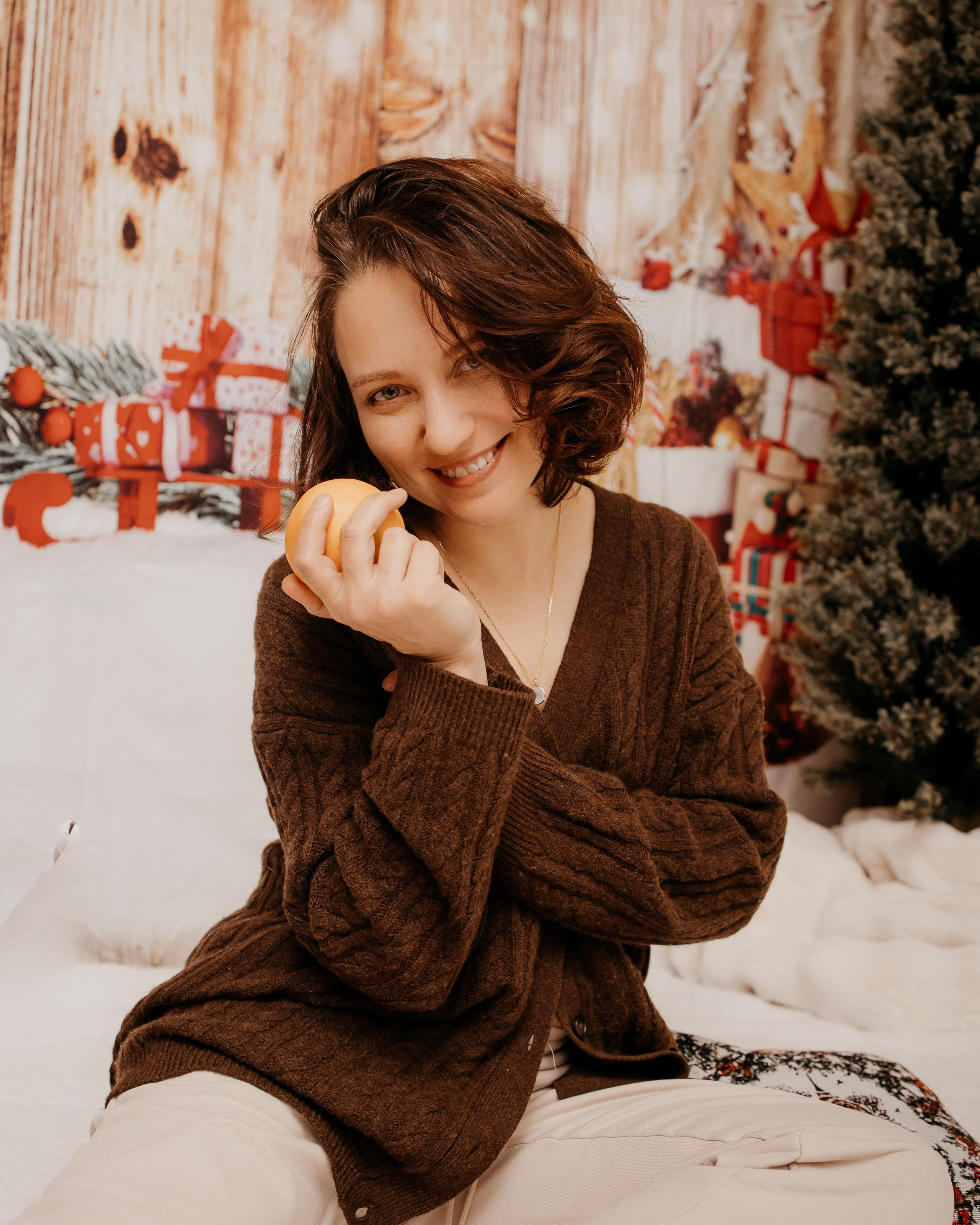 Cozy Christmas portrait of a smiling woman in a brown sweater holding a mandarin orange.
