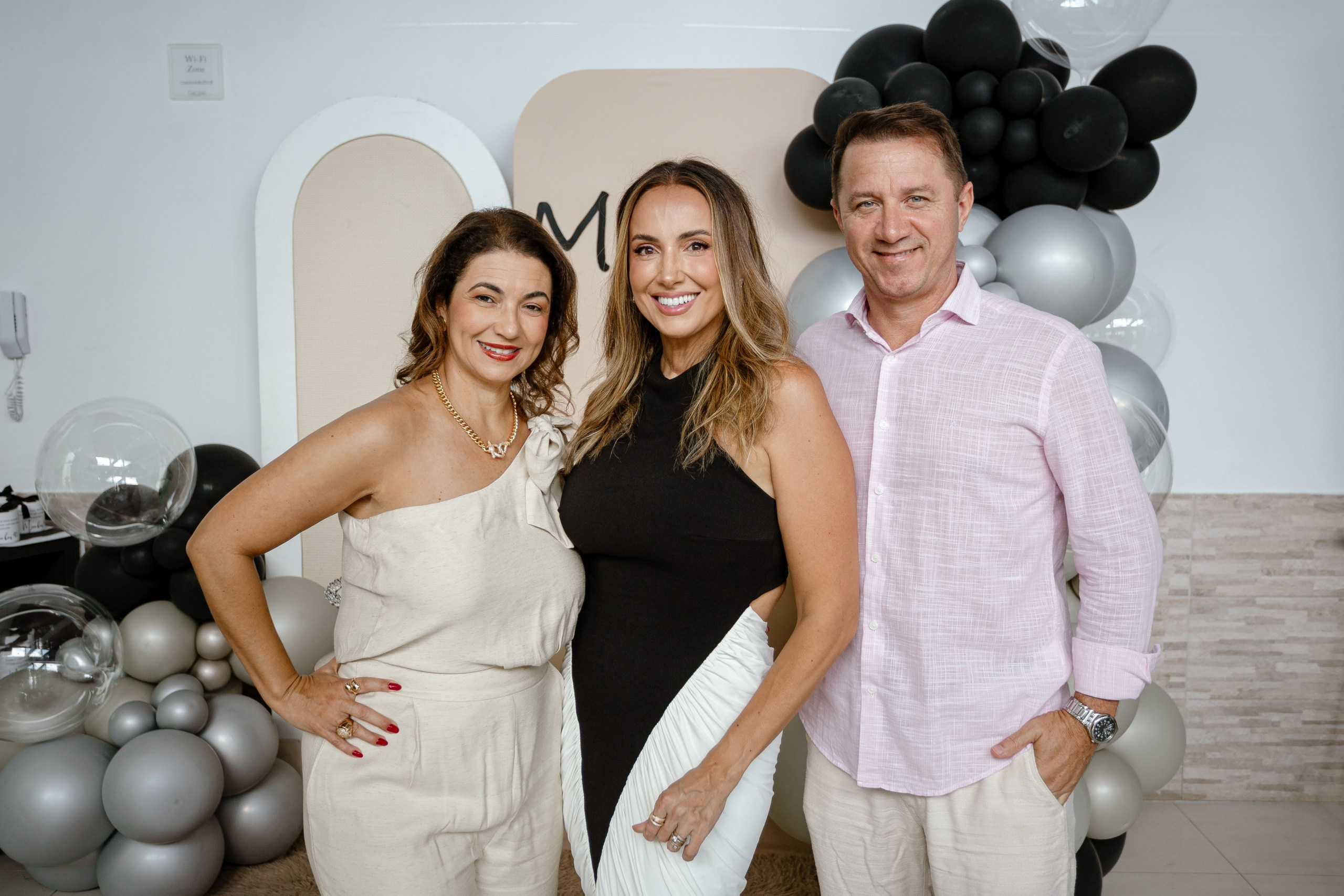 Fotografia de cobertura de festa de aniversário em Itajaí mostrando a aniversariante sorridente posando ao lado de convidados em frente a um painel decorado com balões.