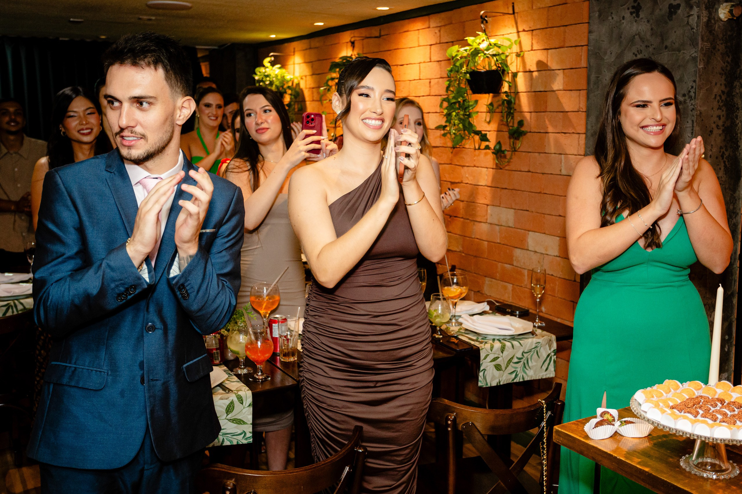 Fotógrafo de formatura em Balneário Camboriú; convidados sorridentes aplaudem animados ao redor da mesa com doces durante a celebração do evento.