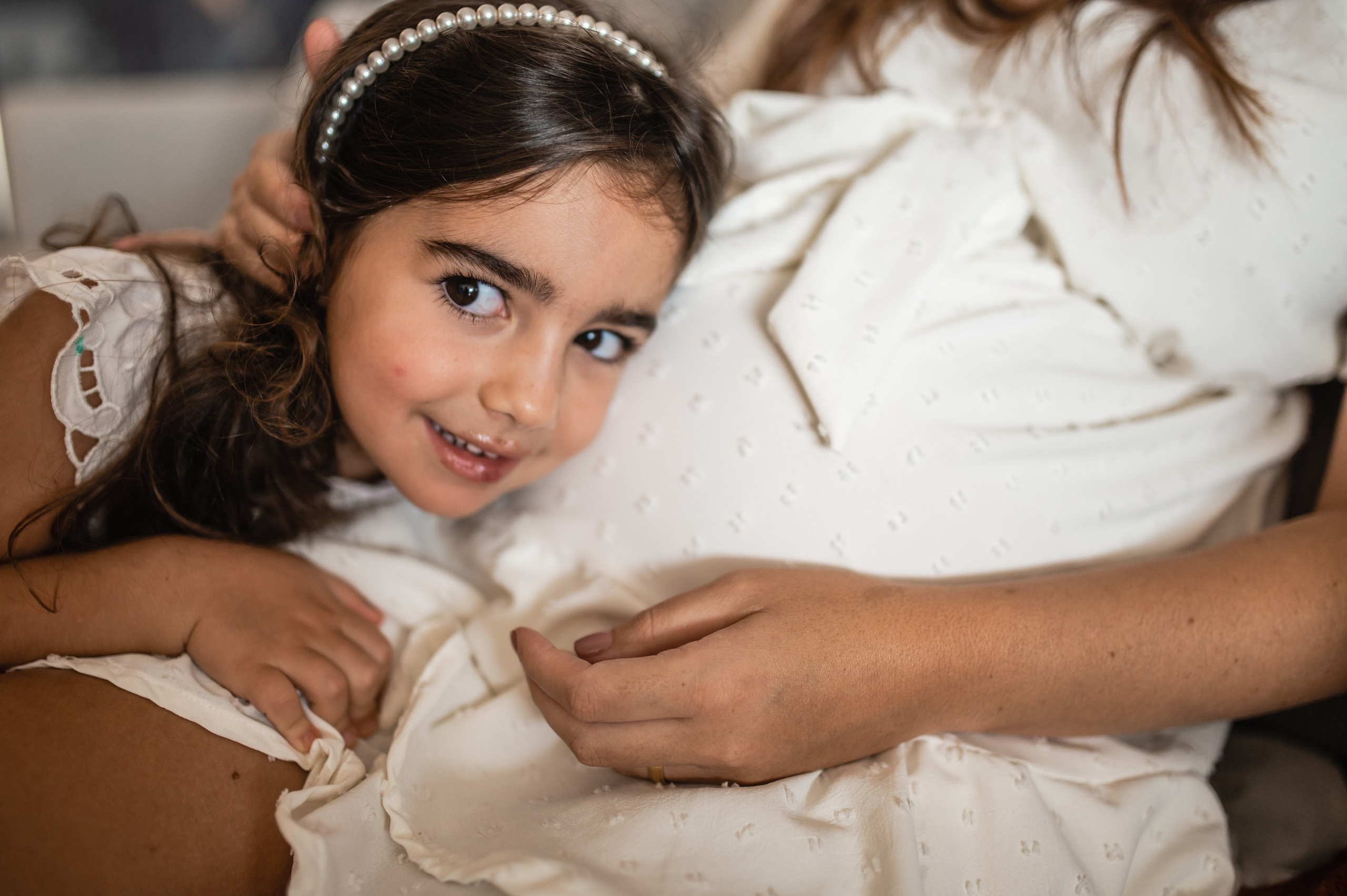 Ensaio gestante com filha em Juiz de Fora, menina encostada na barriga da mãe olhando para câmera