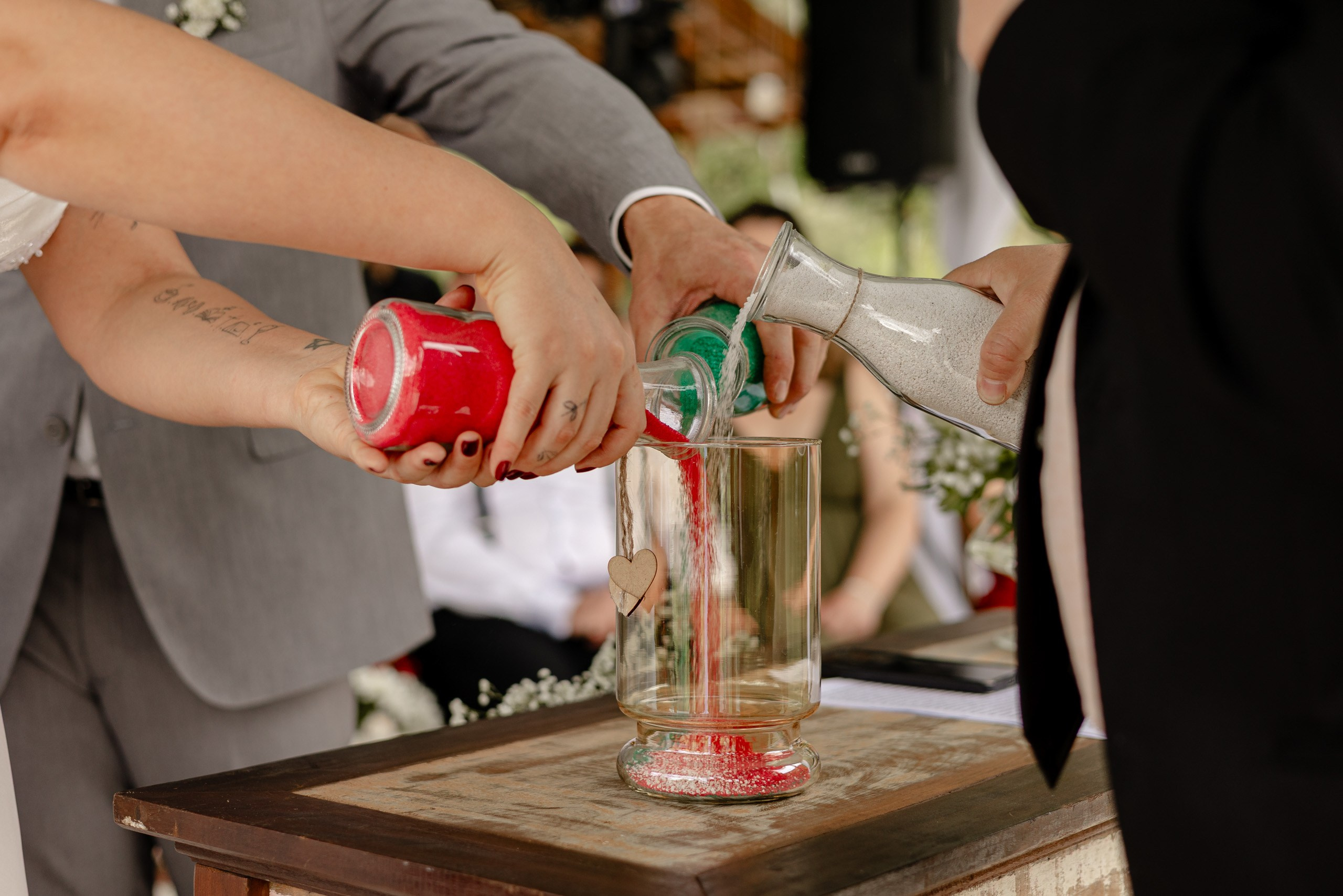 Fotógrafo de casamento em Santa Catarina; ritual das areias com os noivos derramando areias coloridas em um recipiente durante a cerimônia no campo.