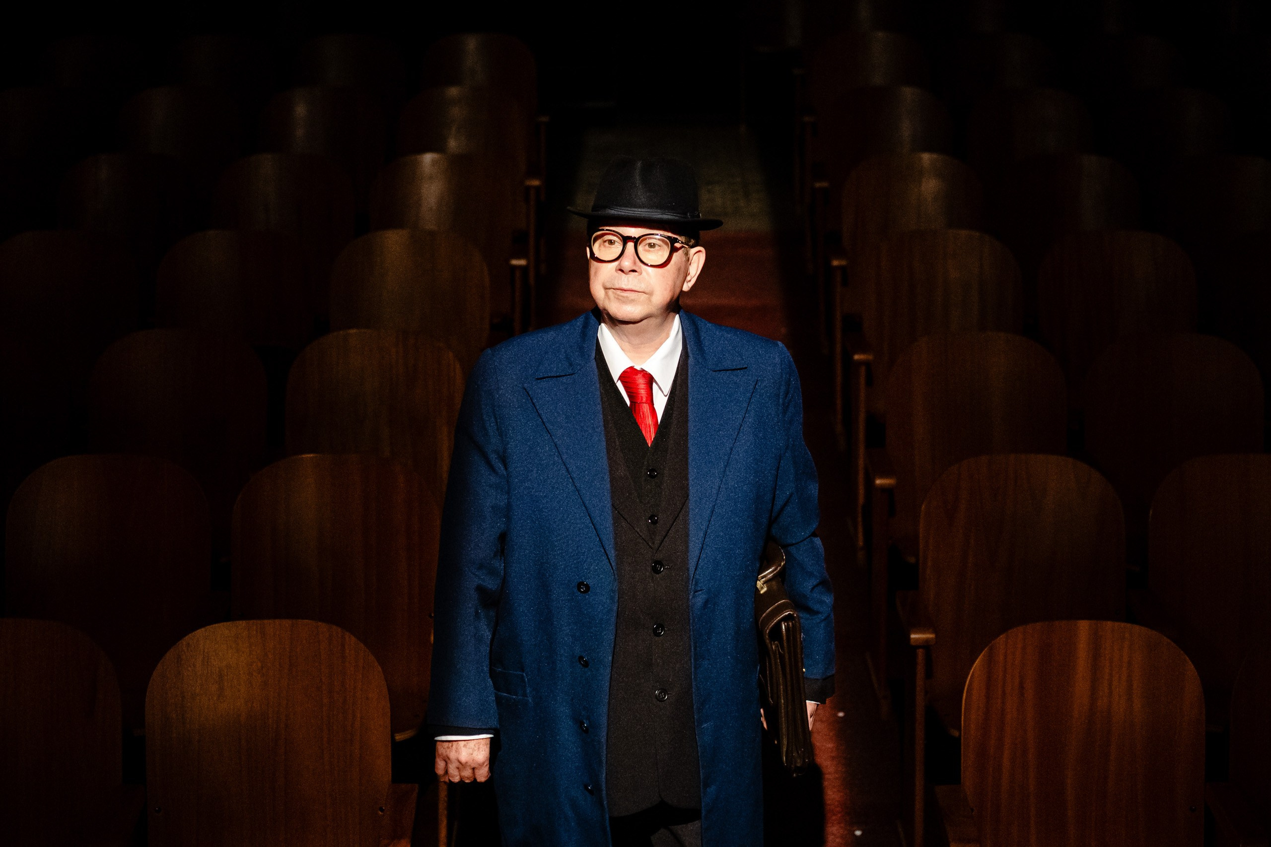 Apresentação teatral com ator em meio a cadeiras do teatro.